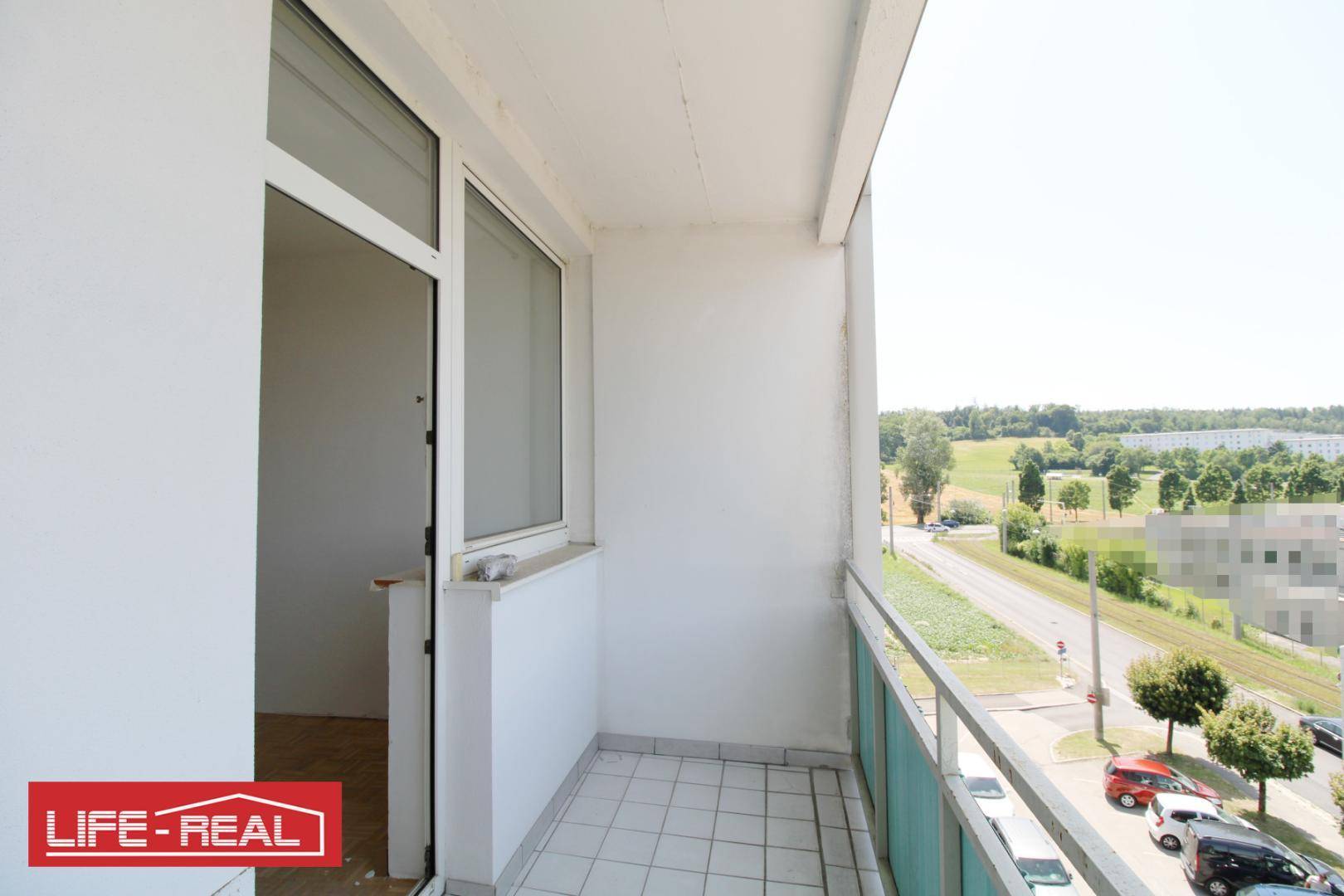 Heller Balkon mit Fliesenboden und Blick auf die Umgebung und viel Grün.
