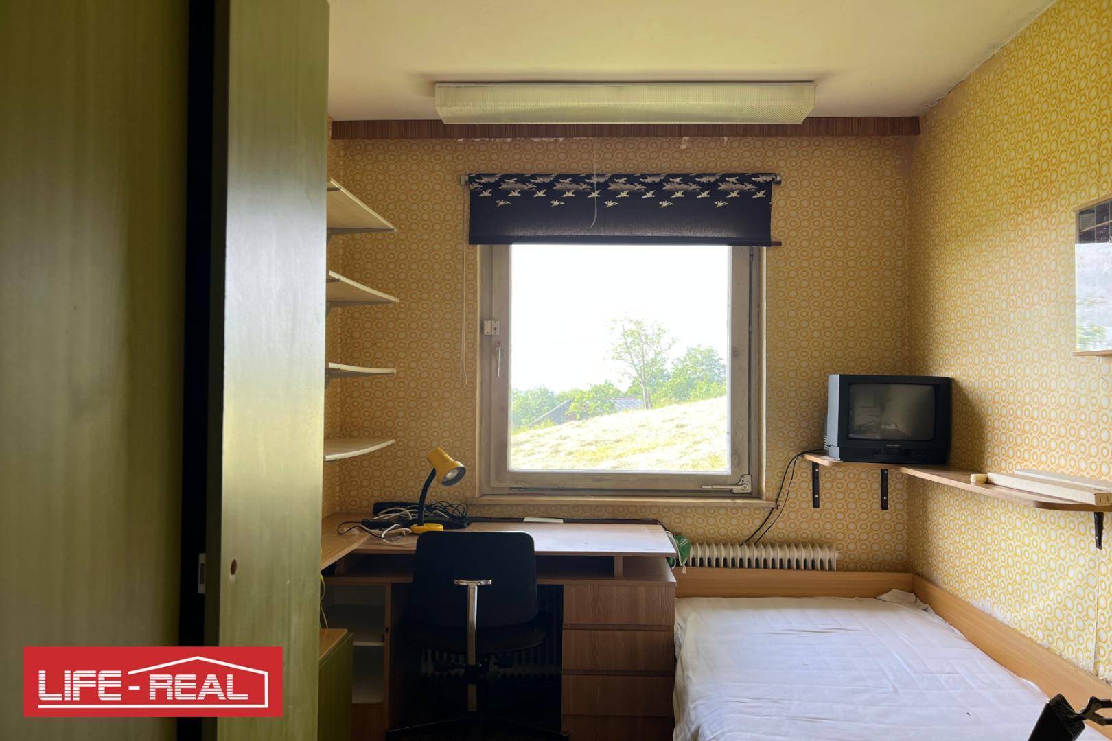 Kleines Schlafzimmer oder Büro mit Bett, Schreibtisch und gemusterter Tapete.