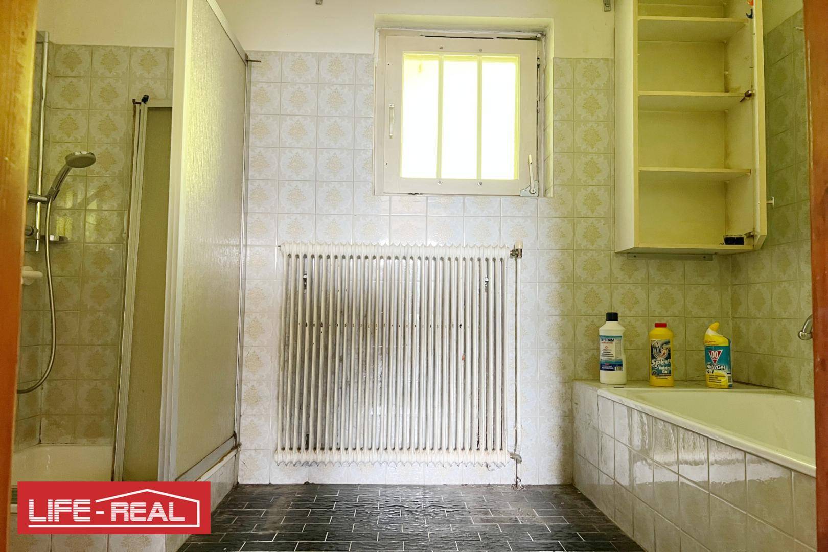Helles Badezimmer mit weißen Fliesen, Dusche, Badewanne und Fenster.
