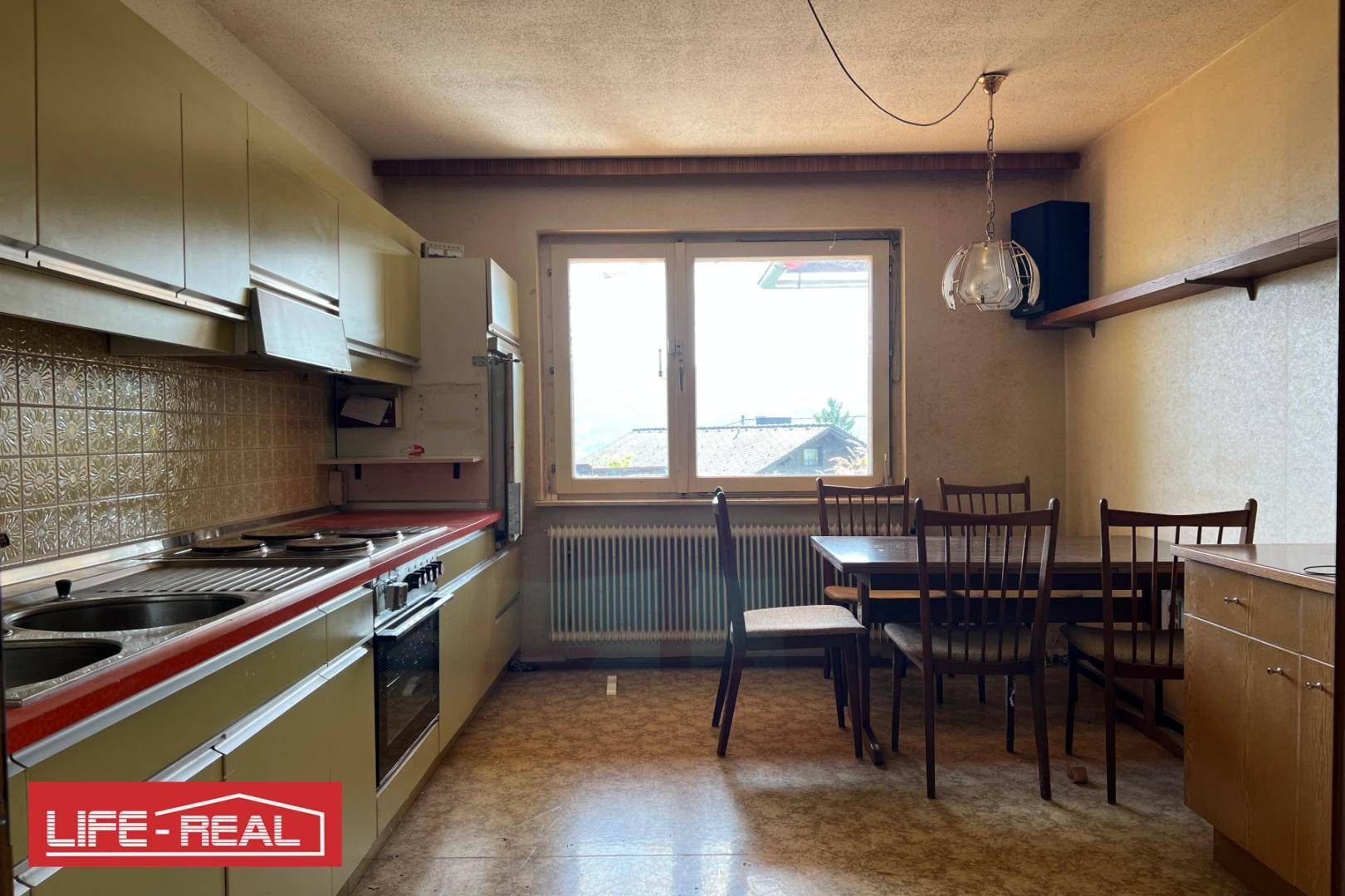 Wohnküche mit hellgrünen Schränken, Esstisch und Fenster, bietet Platz für Mahlzeiten.