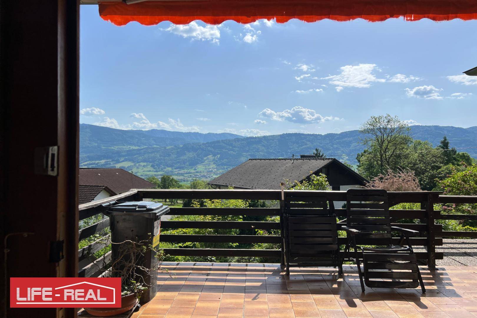 Geräumige Terrasse mit Fliesenboden, Markise und einem beeindruckenden Panoramablick auf die Berge.