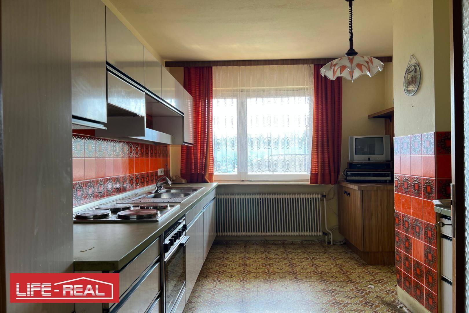 Küche im Retro-Stil mit orange-gemusterten Fliesen, weißen Hängeschränken und Fenster.