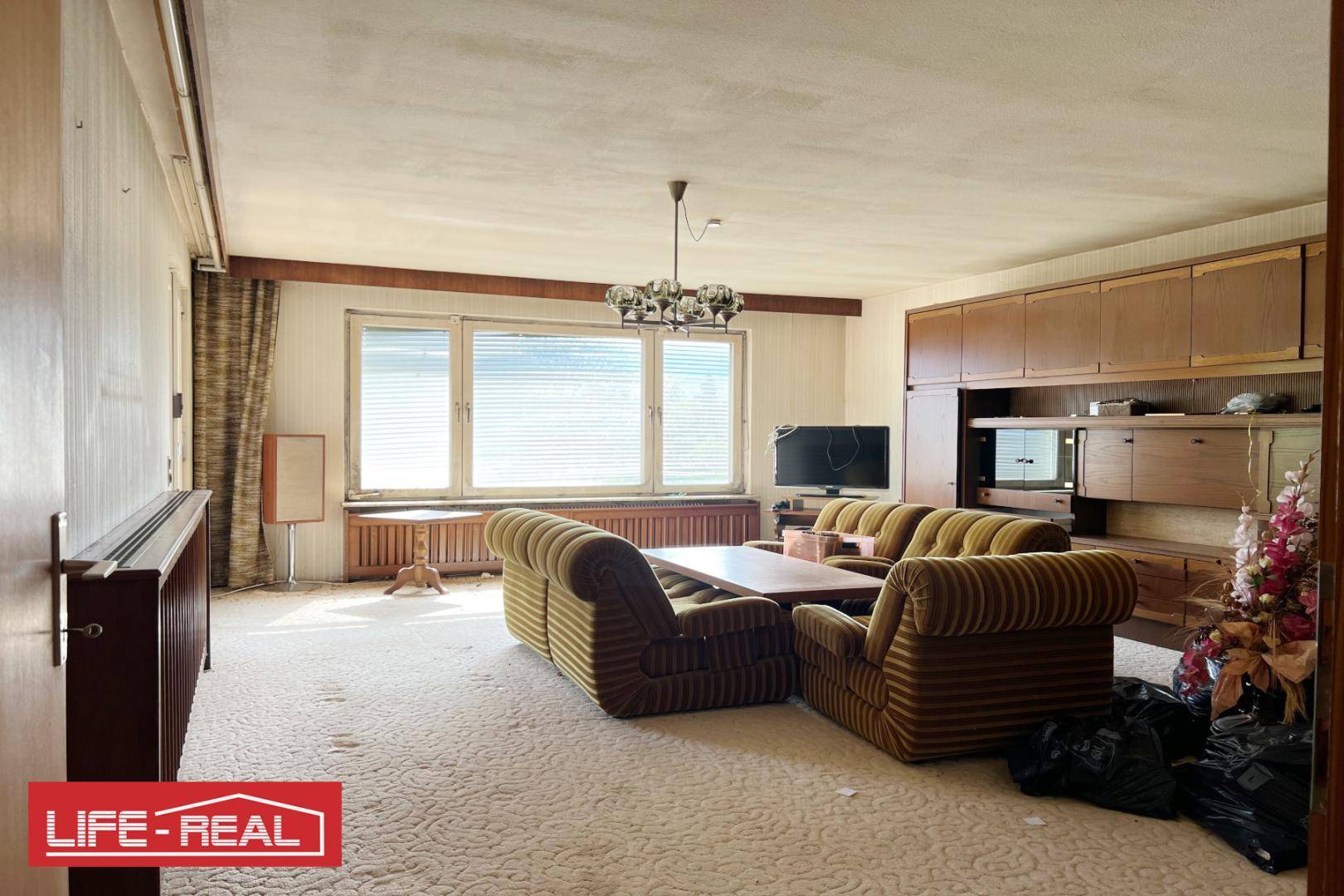 Geräumiges Wohnzimmer mit gestreiften Sofas, großen Fenstern und integrierten Holzschränken.