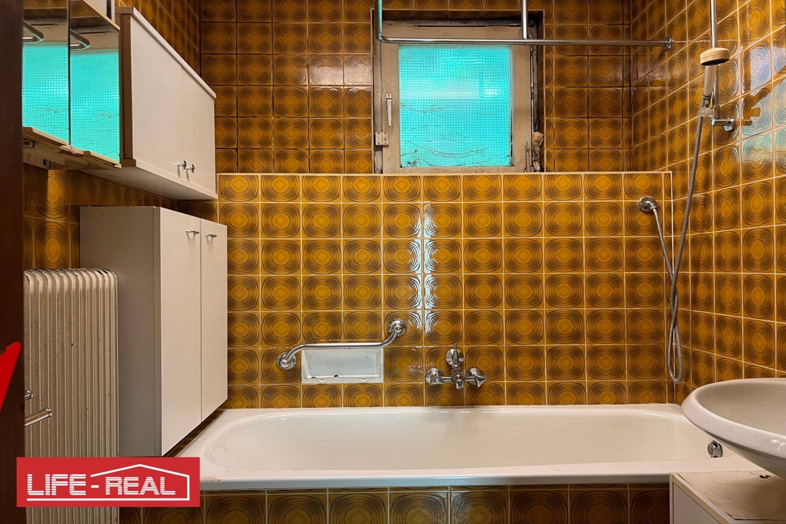Badezimmer mit braunen, gemusterten Fliesen, Badewanne und kleinem Fenster.