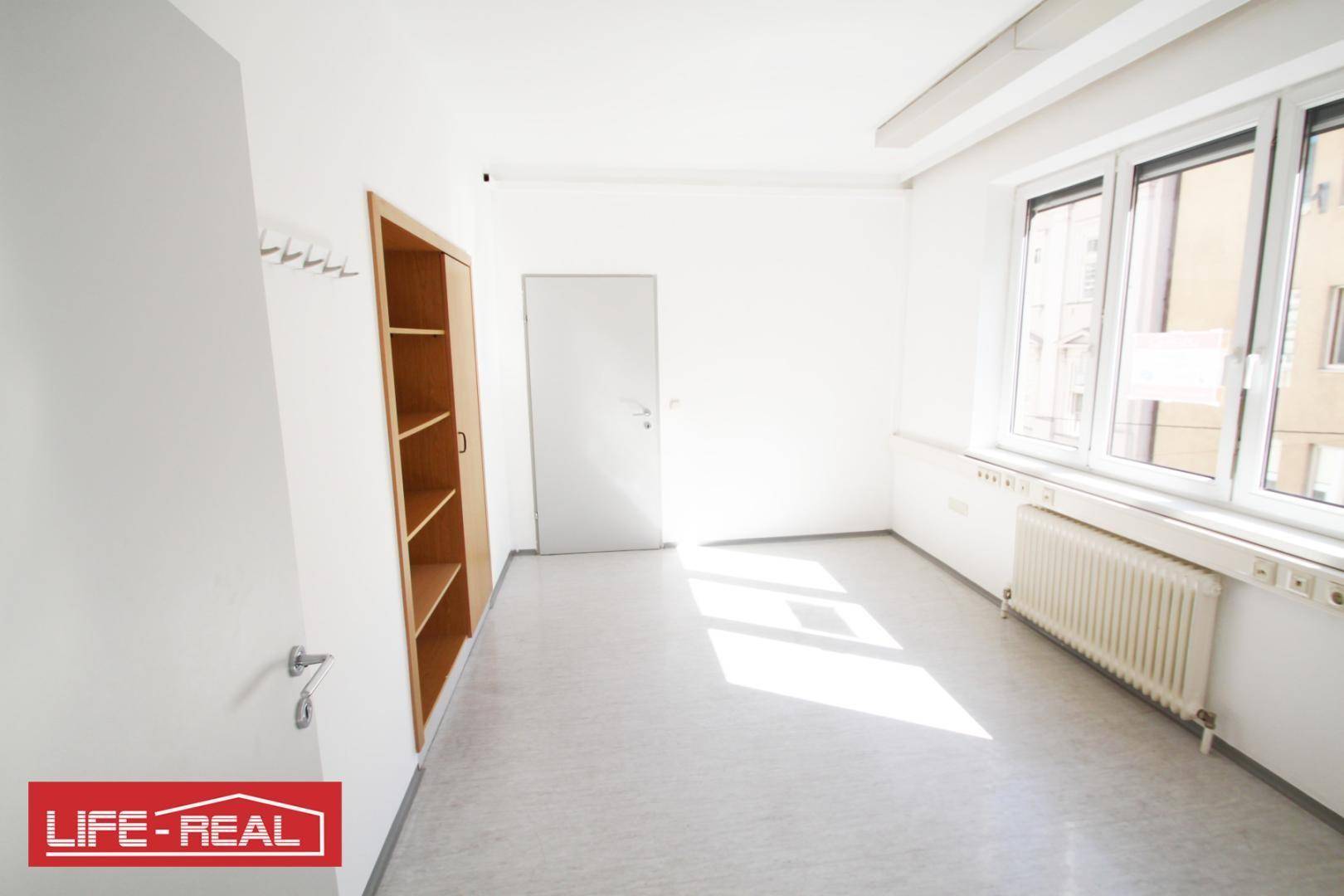 Freundlicher Büroraum mit Fenster, Heizung und einem praktischen Einbauregal aus Holz.