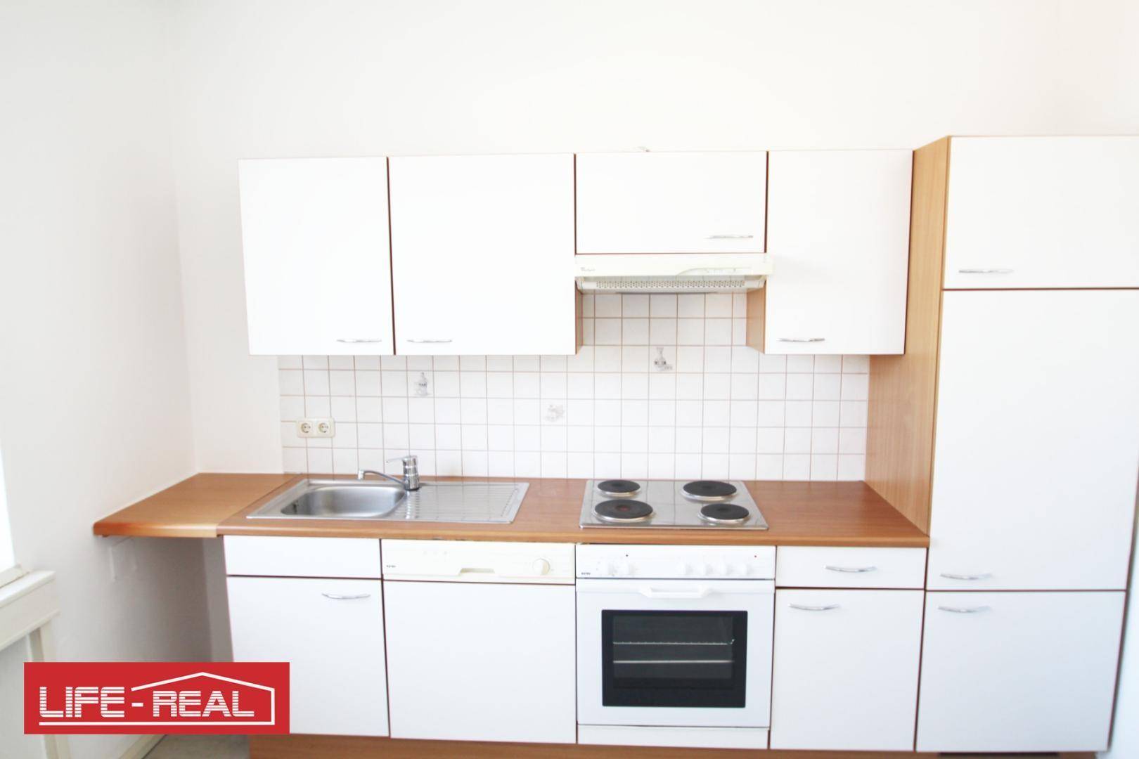 Funktionale Küchenzeile mit weißen Schränken, Holz-Arbeitsplatte und grundlegenden Geräten.
