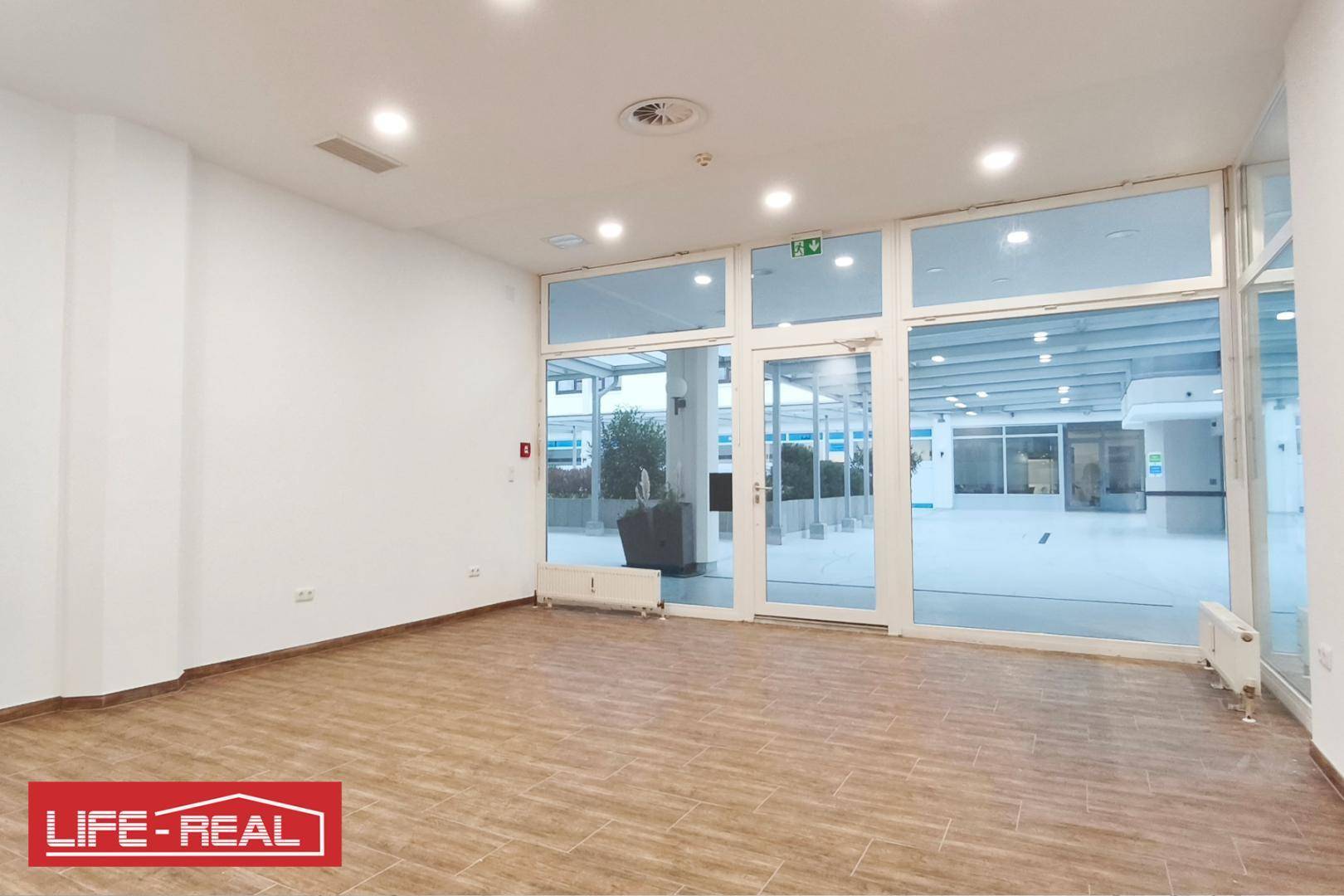 Geräumiger Geschäftsraum mit großen Fensterfronten, die den Blick auf einen Außenbereich freigeben.