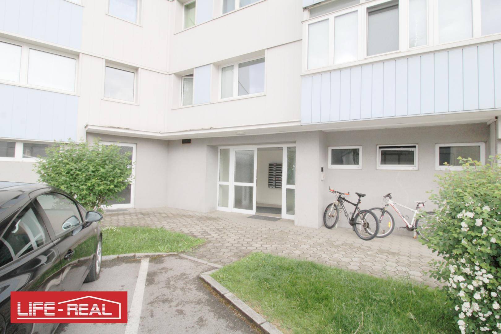 Eingangsbereich eines Wohngebäudes mit Parkplätzen und Fahrradständern.