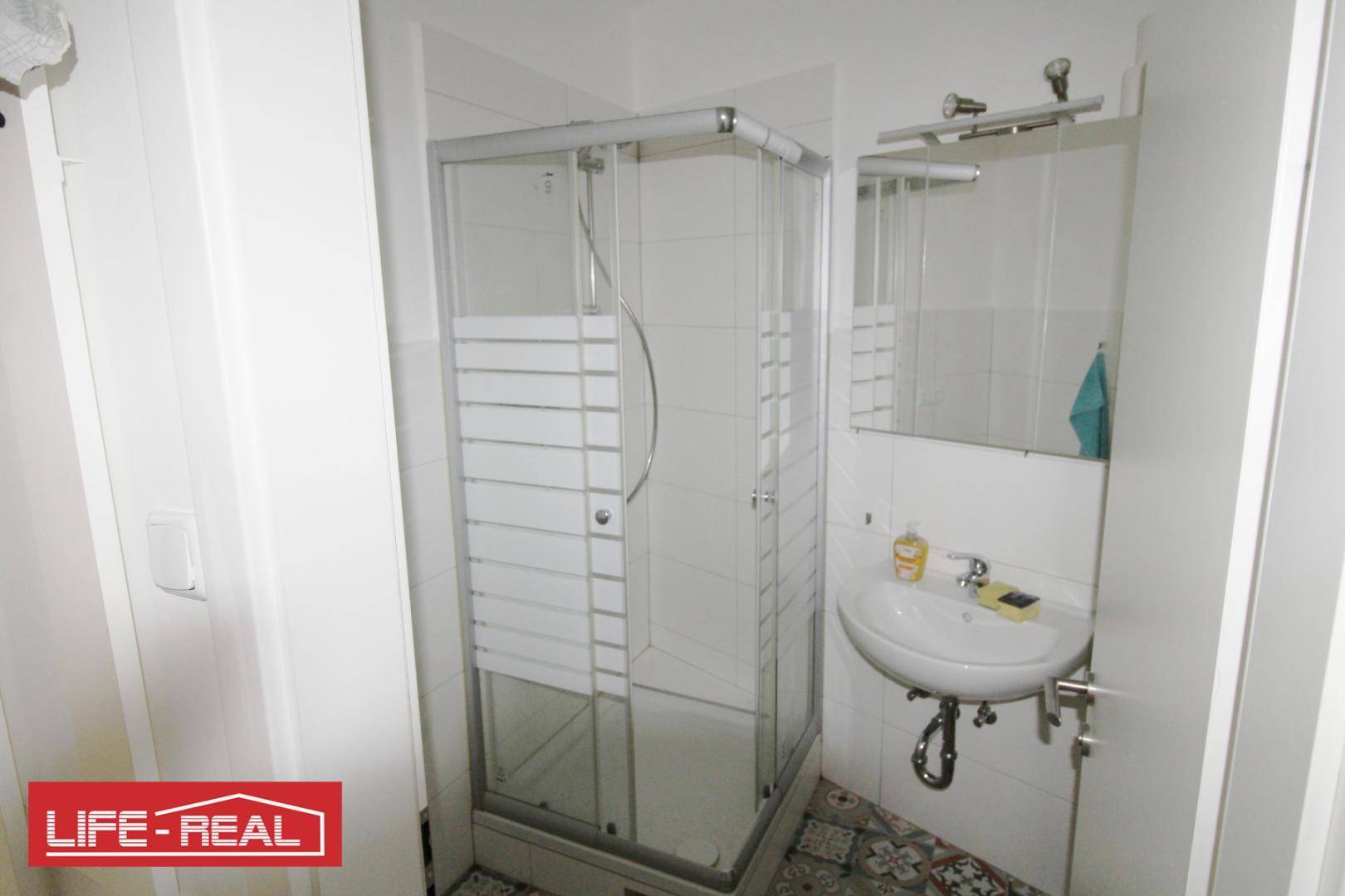 Kleines Badezimmer mit Duschkabine, Waschbecken und gemusterten Fliesen.