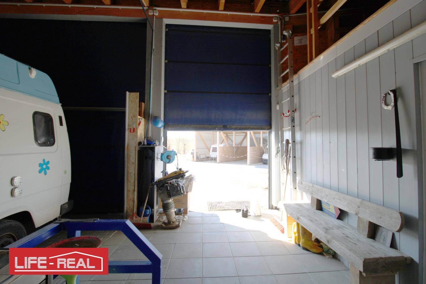 Große Garage oder Werkstatt mit einem offenen blauen Rolltor, einem Lieferwagen und einer Holzbank.