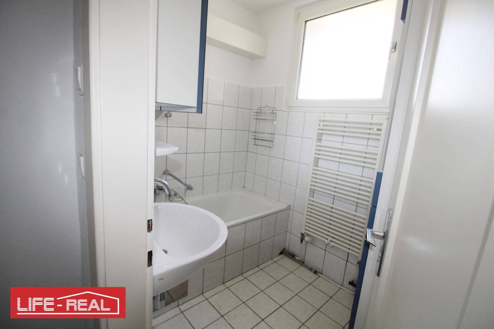 Helles Badezimmer mit Badewanne, Waschbecken, beheiztem Handtuchhalter und Fenster.