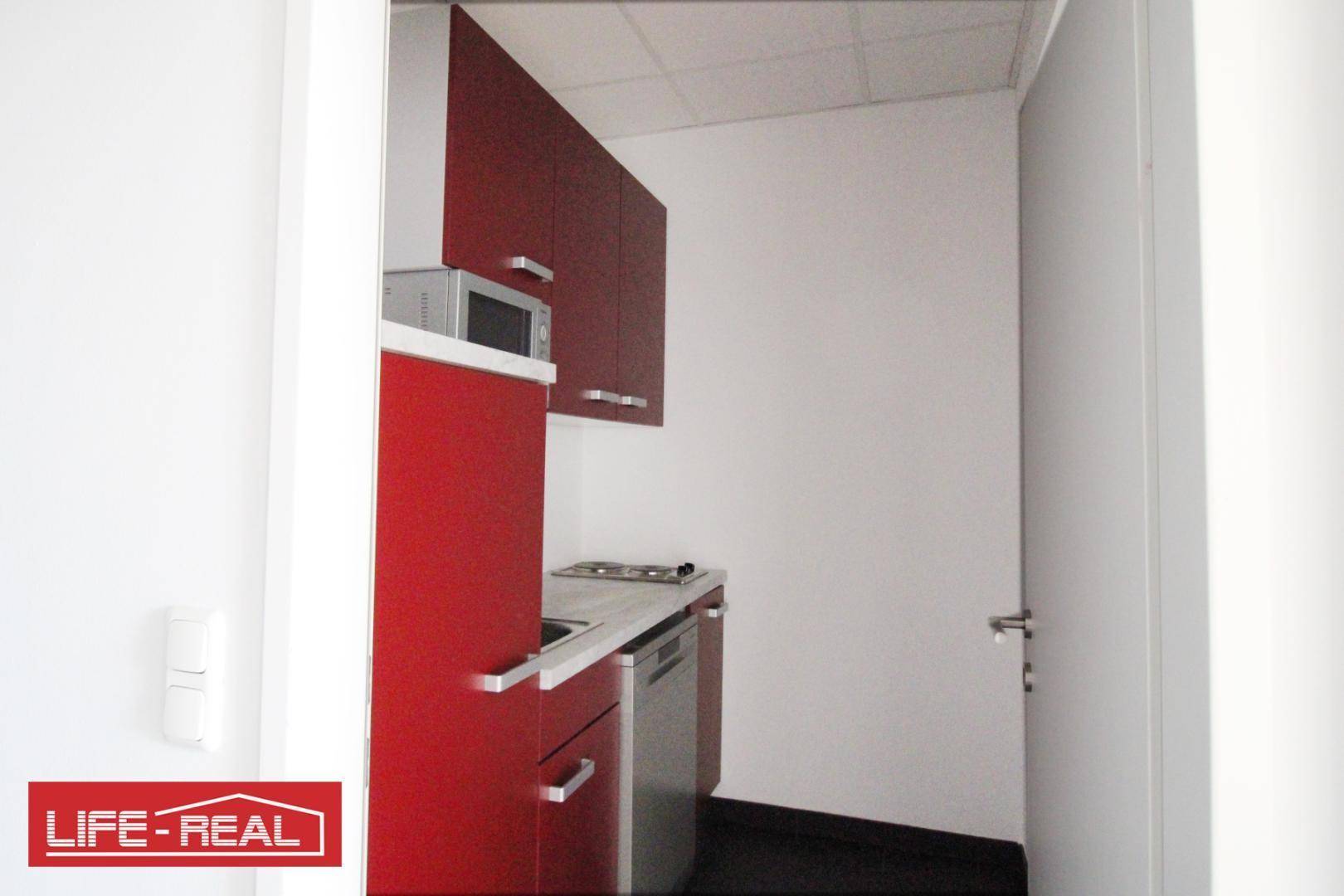 Kompakte Küchenzeile mit leuchtend roten Schränken, Mikrowelle und Kochfeld, ideal für kleine Büros oder Apartments.
