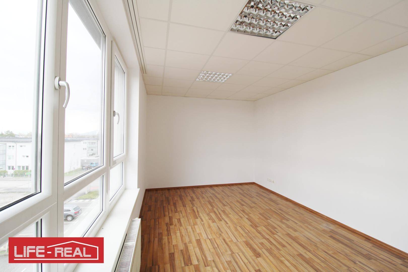 Geräumiges Büro mit großen Fenstern, die einen Blick auf die Umgebung ermöglichen, und hellem Laminatboden.