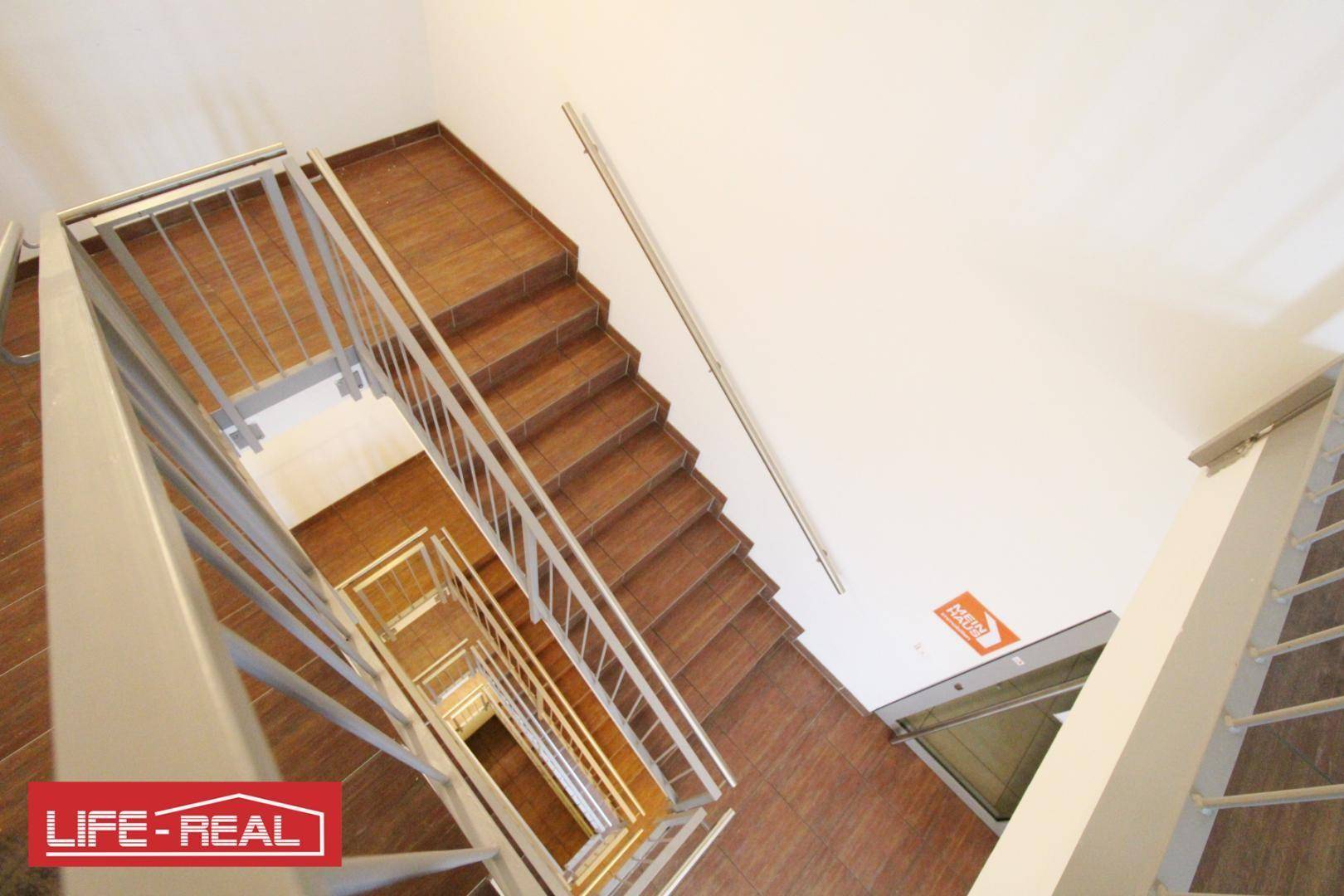 Modernes Treppenhaus mit Metallgeländern und Holzstufen, das sich über mehrere Etagen erstreckt und gut beleuchtet ist.
