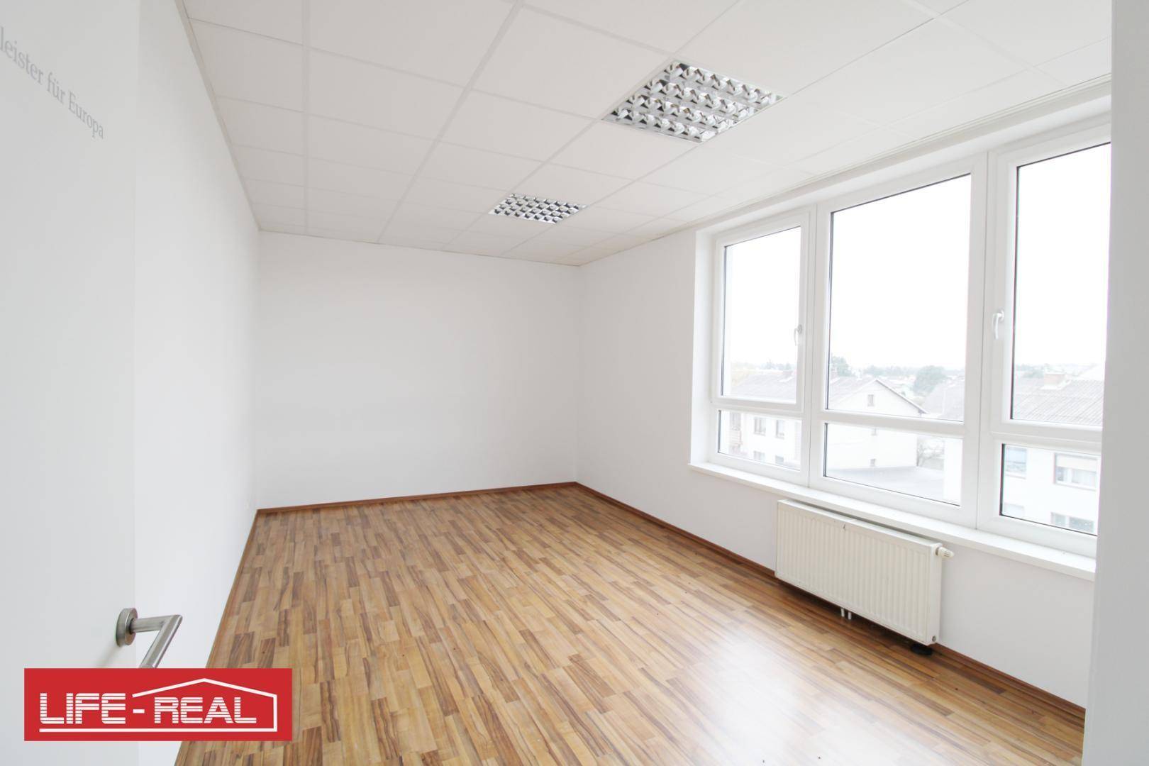 Heller Büroraum mit großen Fenstern, die einen weiten Blick bieten, und einem Heizkörper unter der Fensterbank.