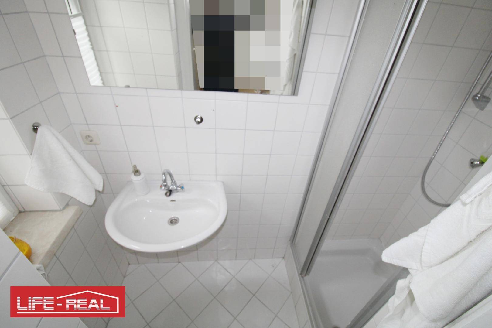 Kleines Badezimmer mit weißen Fliesen, Waschbecken und einer praktischen Duschkabine.