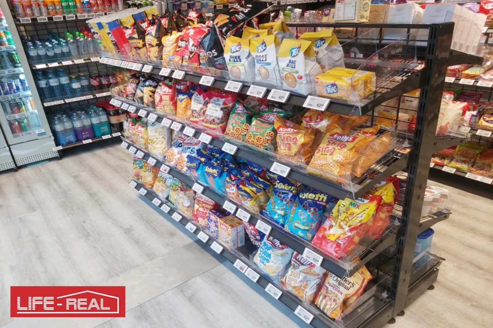 Blick in einen gut sortierten Verkaufsraum mit Regalen voller Snacks und Süßigkeiten auf hellem Boden.