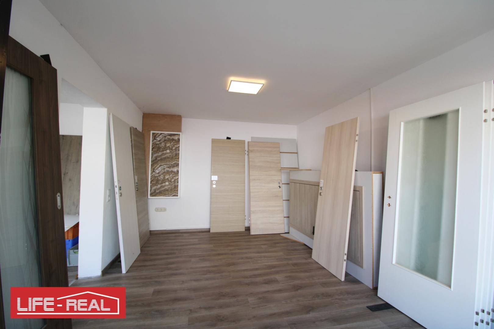 Heller Gewerberaum mit Laminatboden, Deckenleuchte und verschiedenen Türen, die im Raum platziert sind.