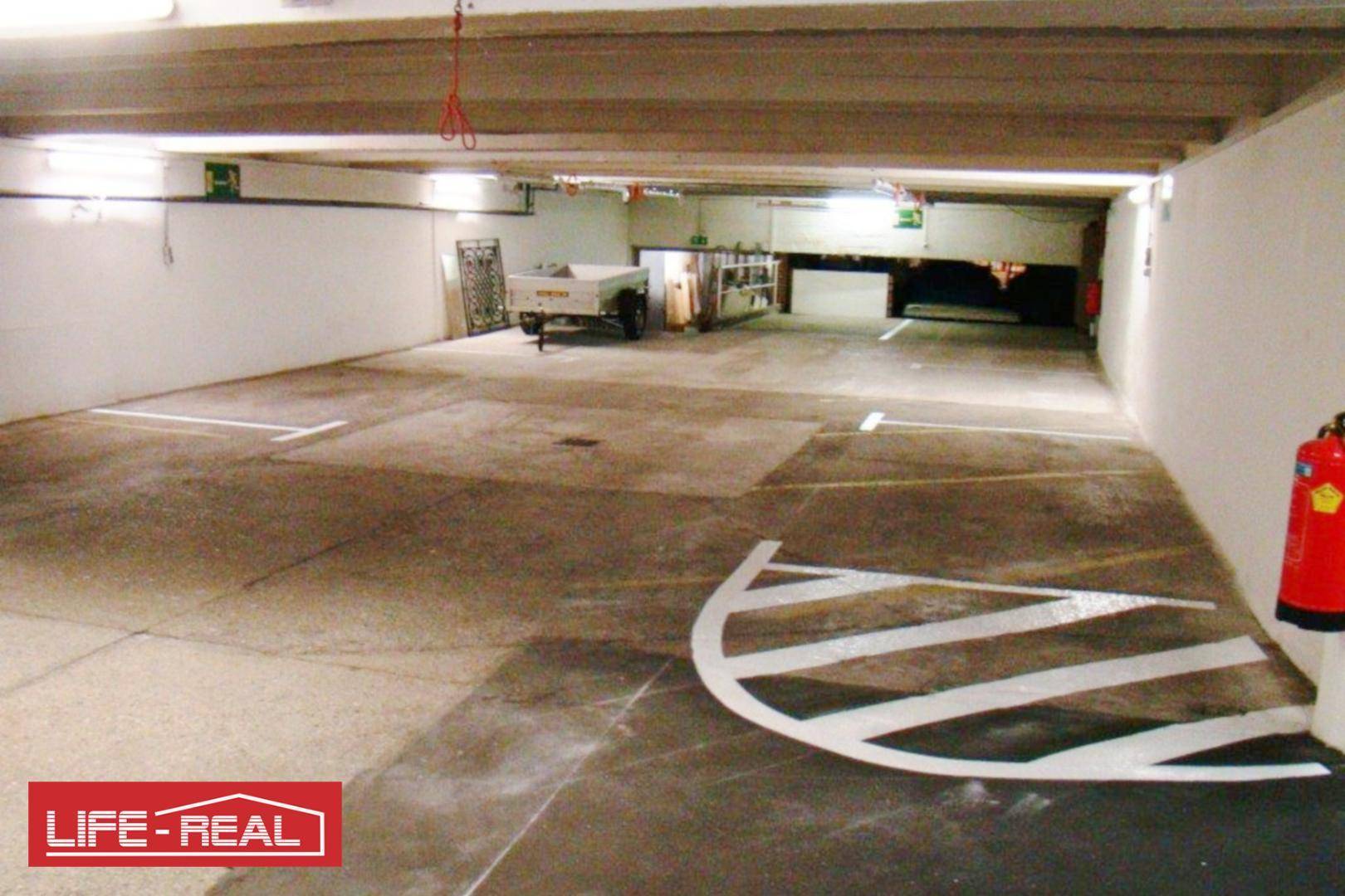 Geräumige Tiefgarage mit Betonboden, Parkplatzmarkierungen und einem Feuerlöscher an der Wand.