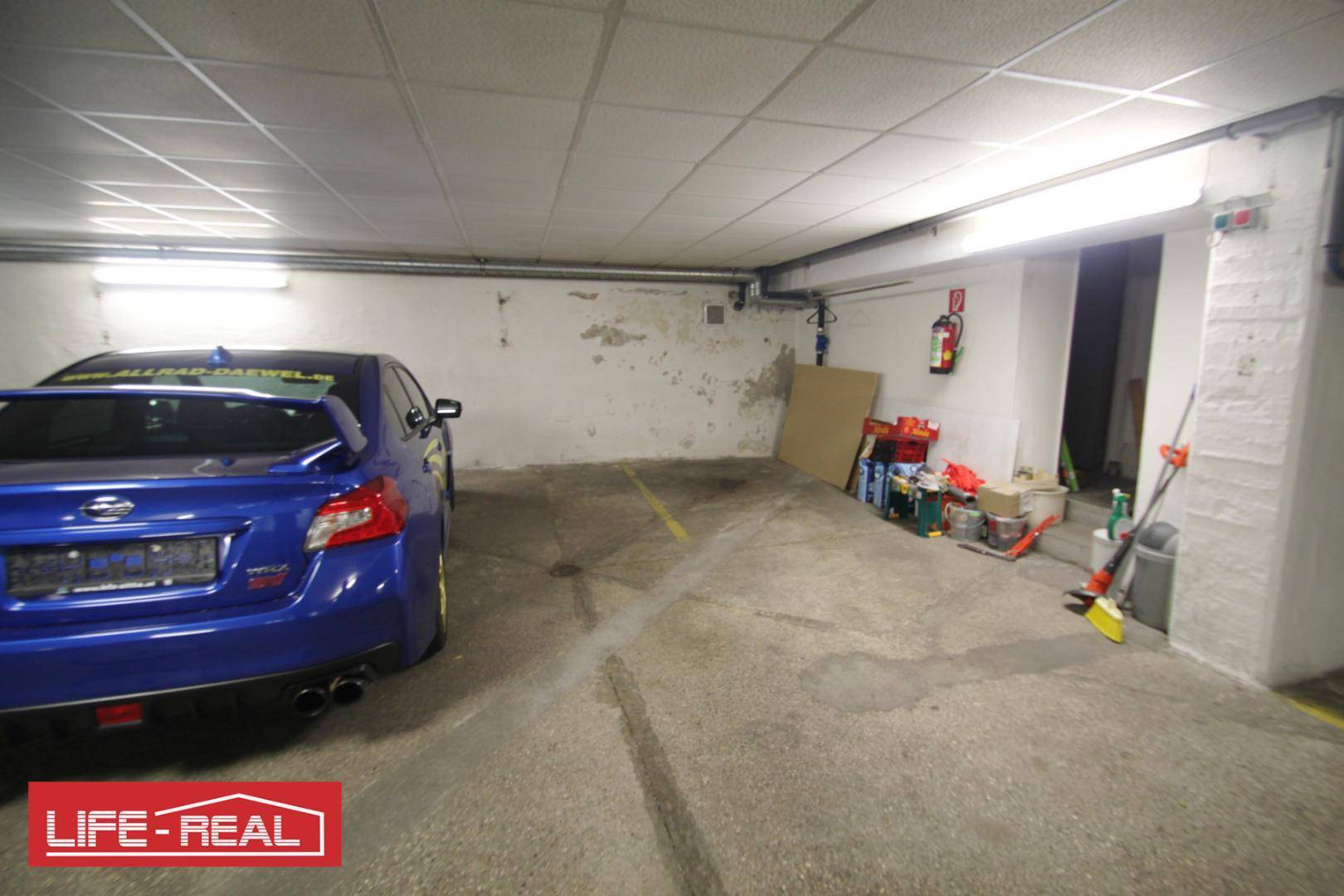 Tiefgarage mit einem blauen Auto, Lagerfläche und einem Feuerlöscher an der Wand.