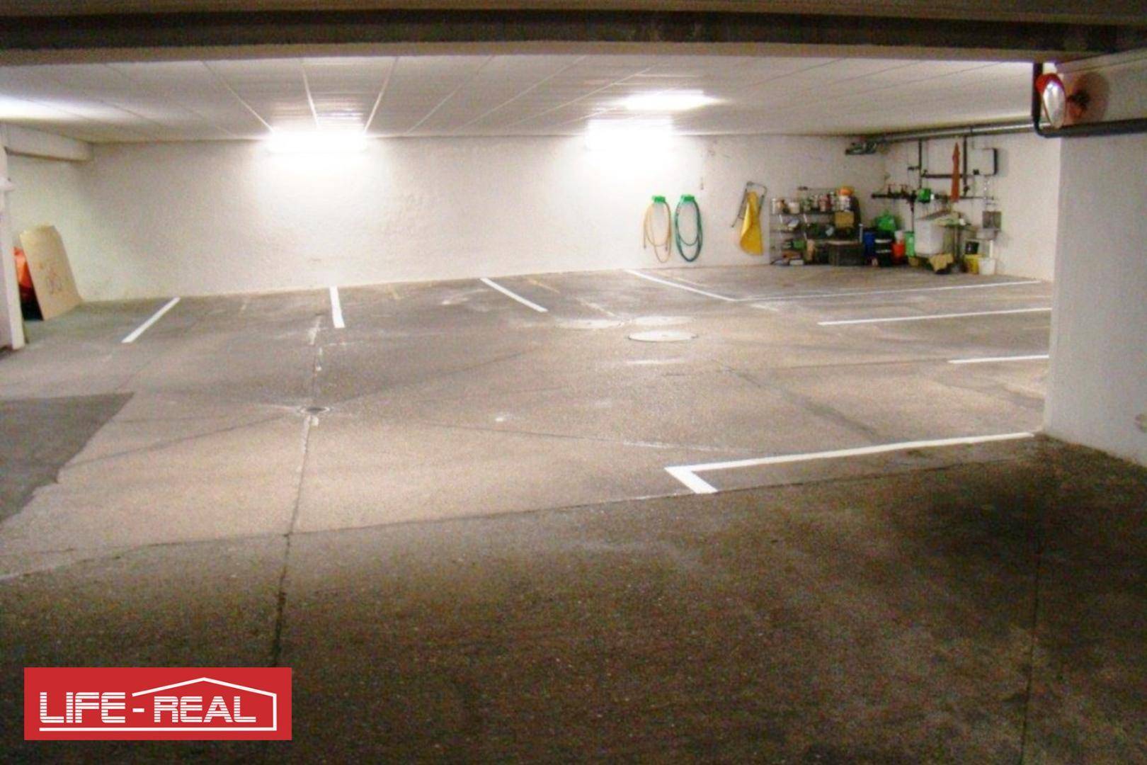 Tiefgarage mit markierten Parkplätzen und Lagerbereich an der Wand unter heller Beleuchtung.