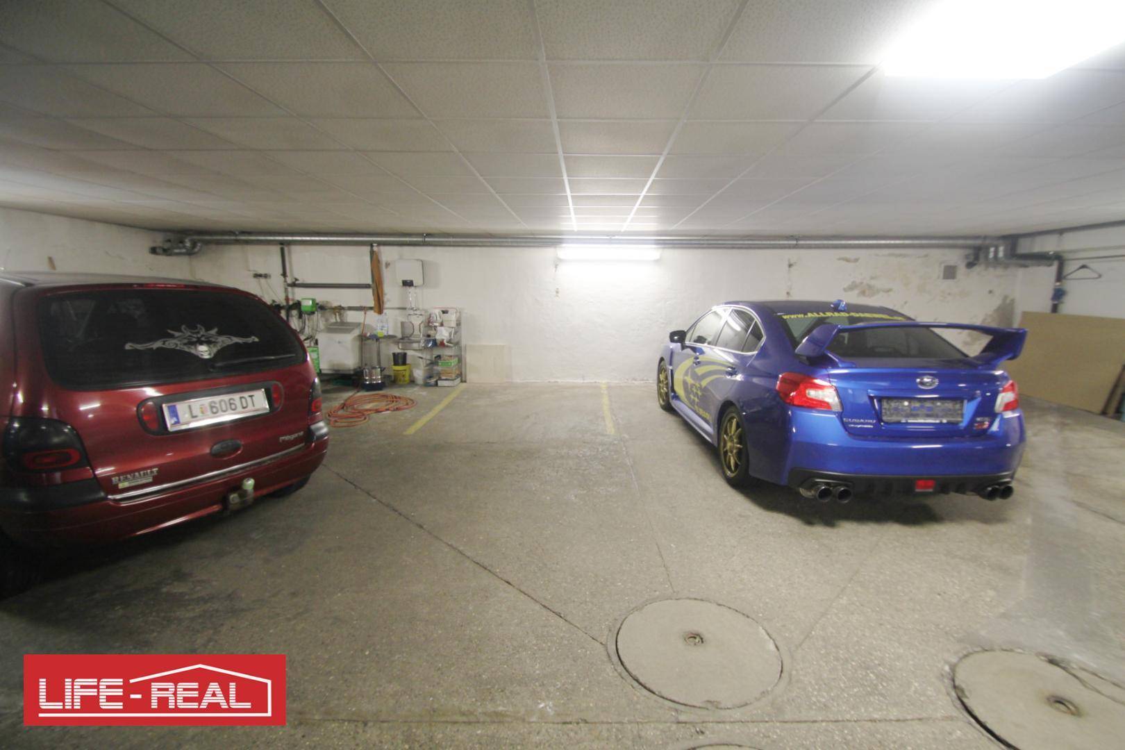 Tiefgarage mit zwei geparkten Autos, Betonboden und Deckenbeleuchtung in einem funktionalen Raum.