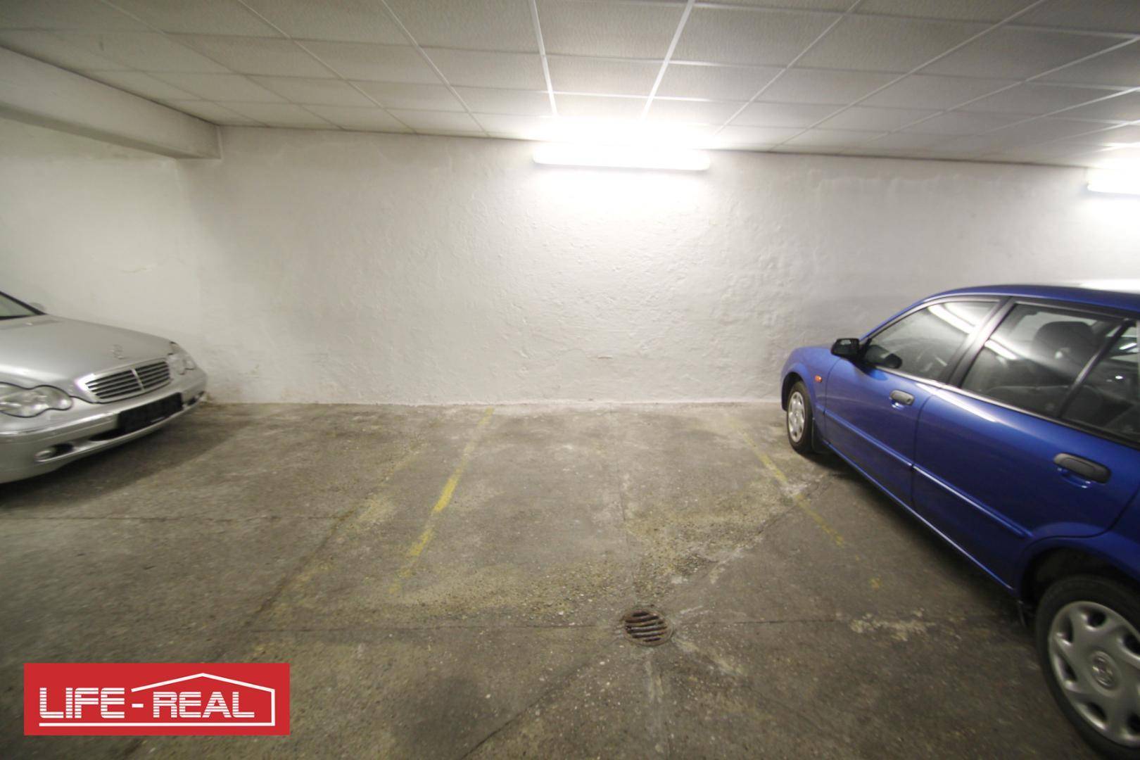 Teilansicht einer Tiefgarage mit einem geparkten Auto und einfacher Deckenbeleuchtung.