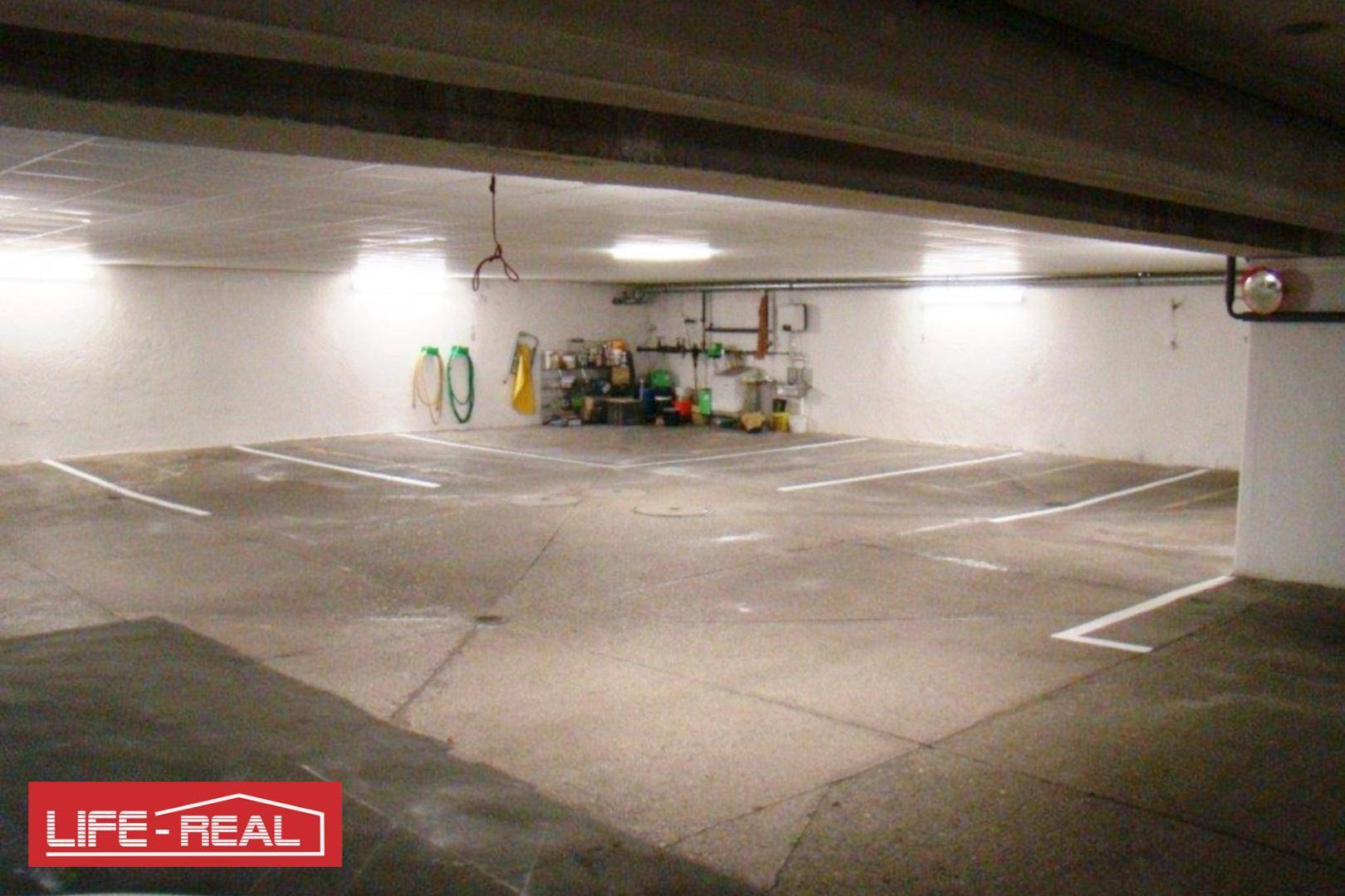 Tiefgarage mit mehreren Parkplätzen, Beleuchtung und einem kleinen Lagerbereich im Hintergrund.