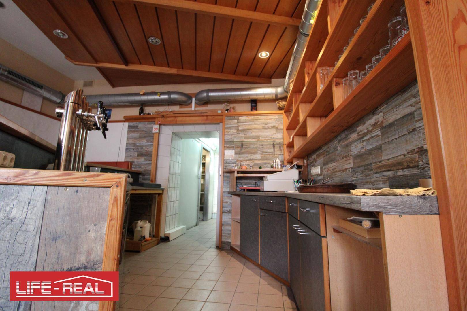 Servicebereich hinter der Bar mit Regalen, Arbeitsflächen und Fliesenboden, bereit für den Gastronomiebetrieb.
