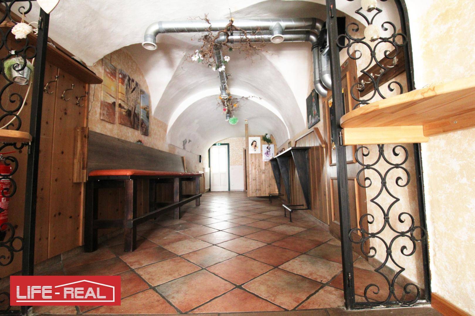 Gewölbter Gangbereich mit Sitzgelegenheiten, dekorativen Elementen und sichtbaren Lüftungsrohren.