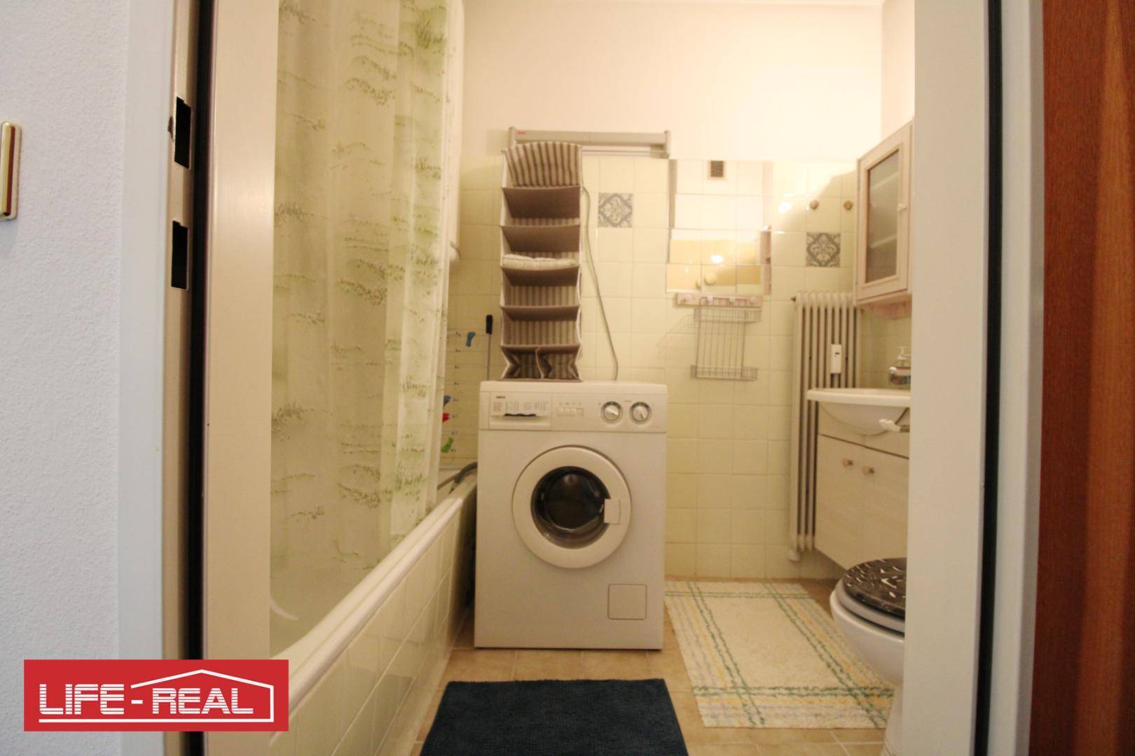 Badezimmer mit Badewanne, Duschvorhang, Waschmaschine und einem Waschbecken mit Spiegelschrank.
