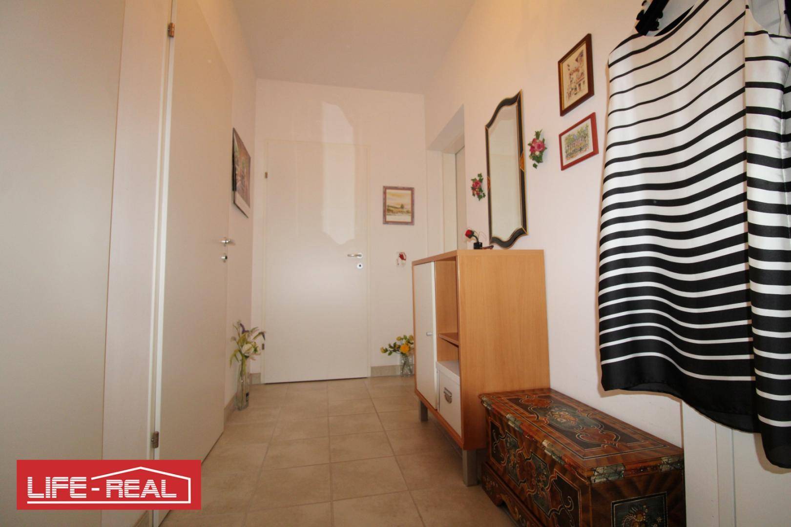 Heller Flur mit Fliesenboden, Garderobe und einem dekorativen Schrank.