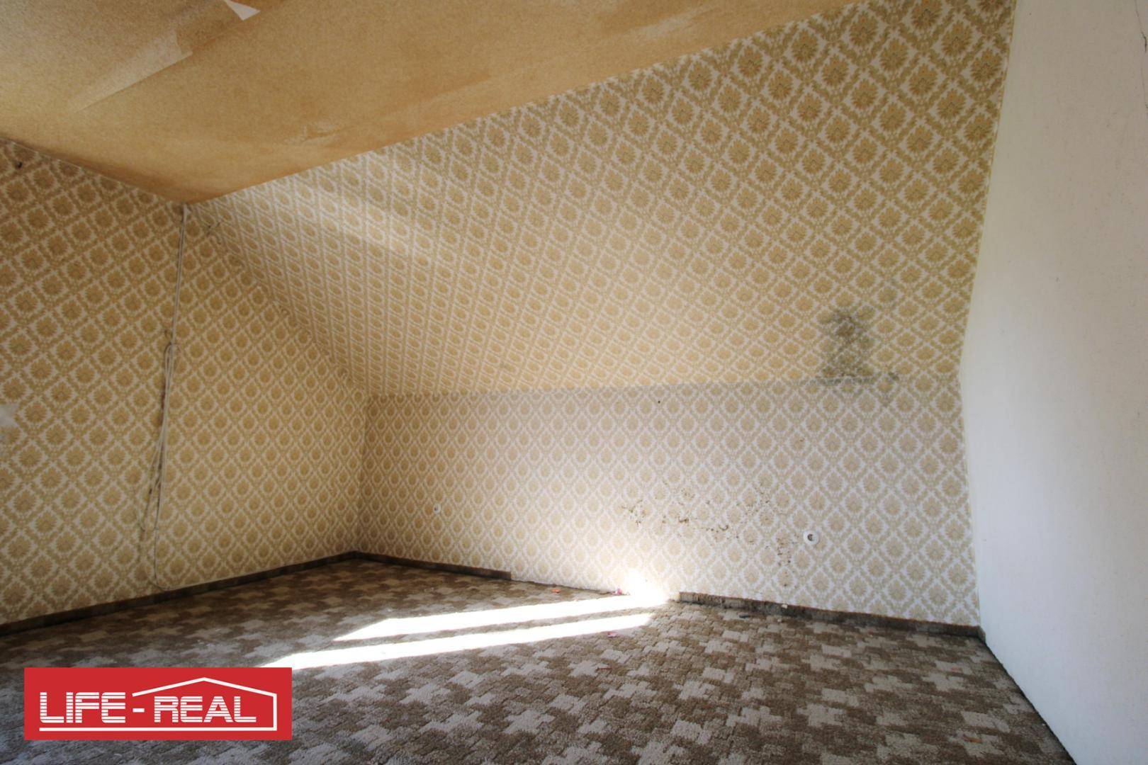 Leeres Zimmer mit gemusterter Tapete und Teppichboden, gekennzeichnet durch eine Dachschräge.