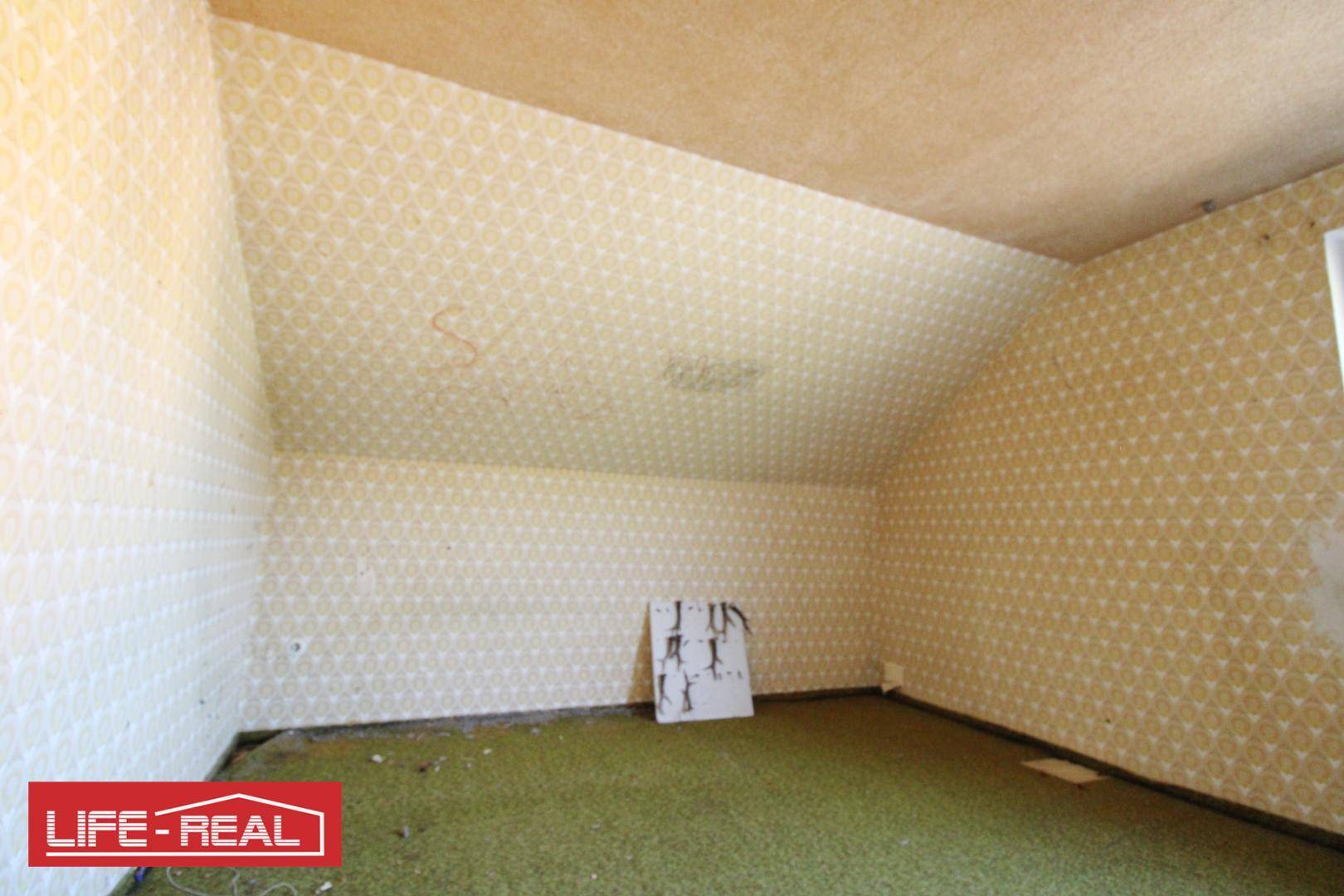 Zimmer mit gemusterter Tapete und grünem Teppichboden, charakterisiert durch eine Dachschräge.