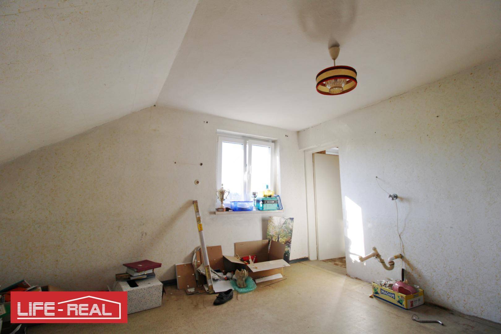 Dachzimmer mit Fenster und schräger Decke, bereit für Renovierung und Neugestaltung.