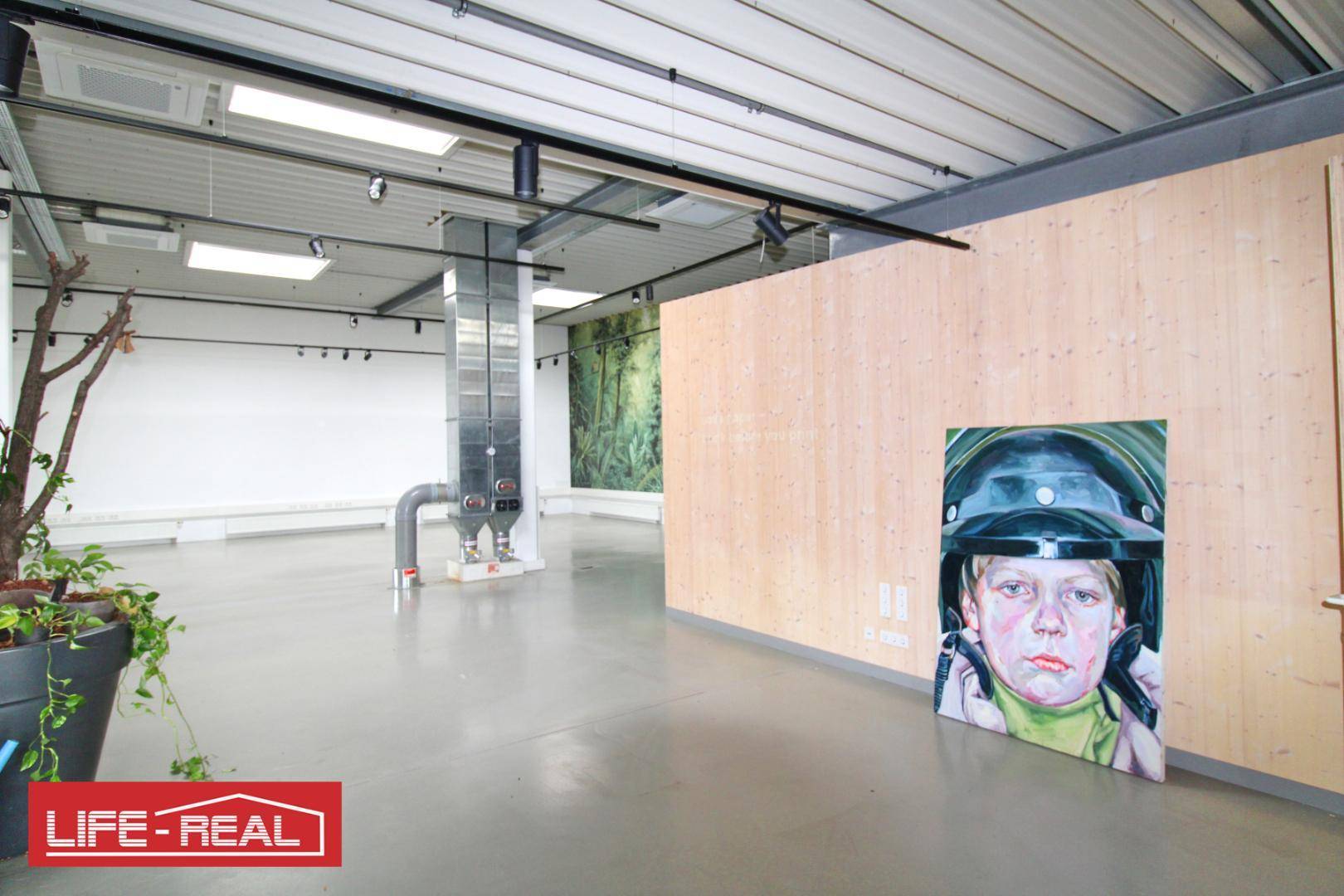 Offener Gewerberaum mit hoher Decke, Betonboden und einer Holzwand mit Kunstwerk.
