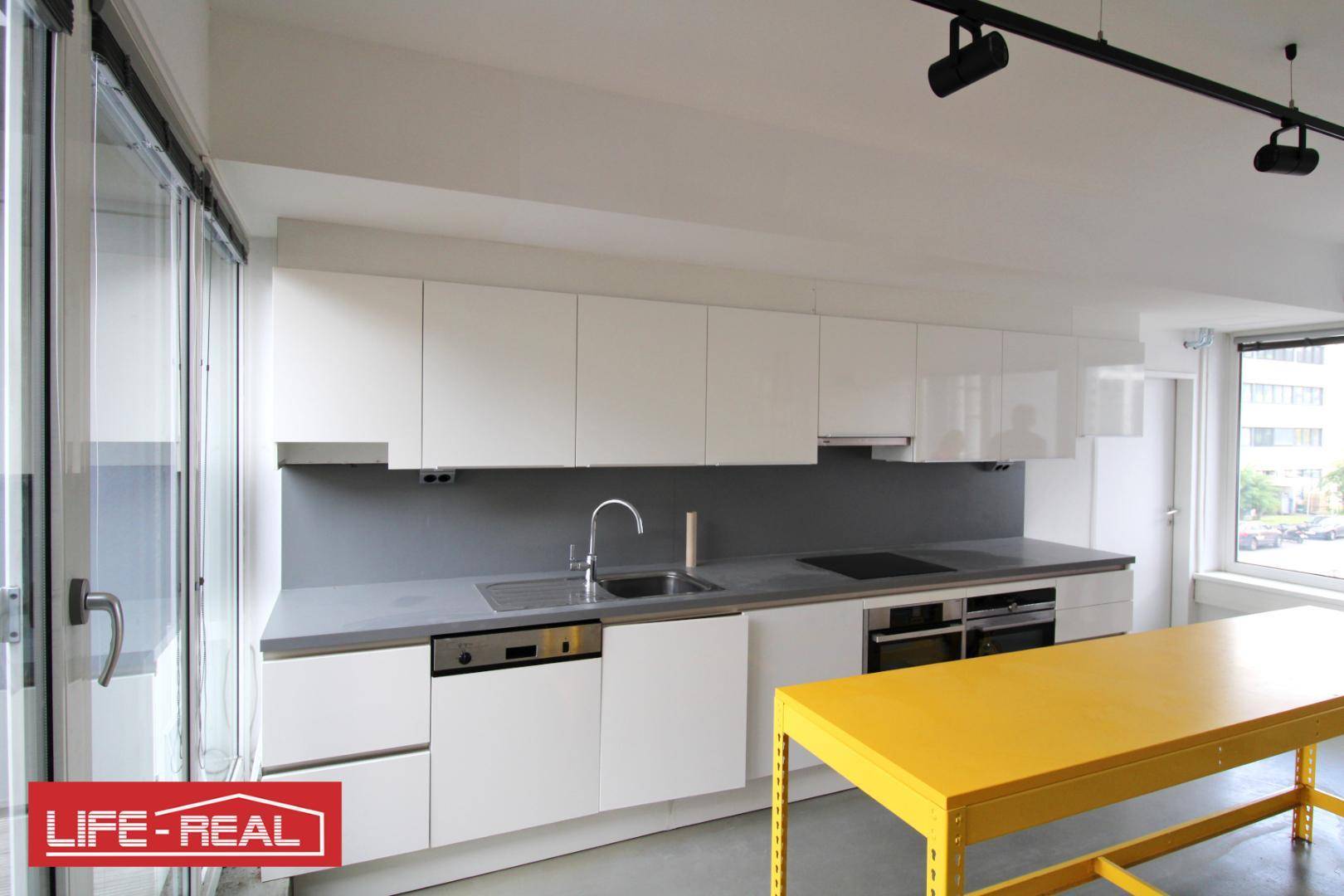 Moderne Einbauküche mit weißen Hochglanzfronten, Spülmaschine und dunkler Arbeitsplatte.