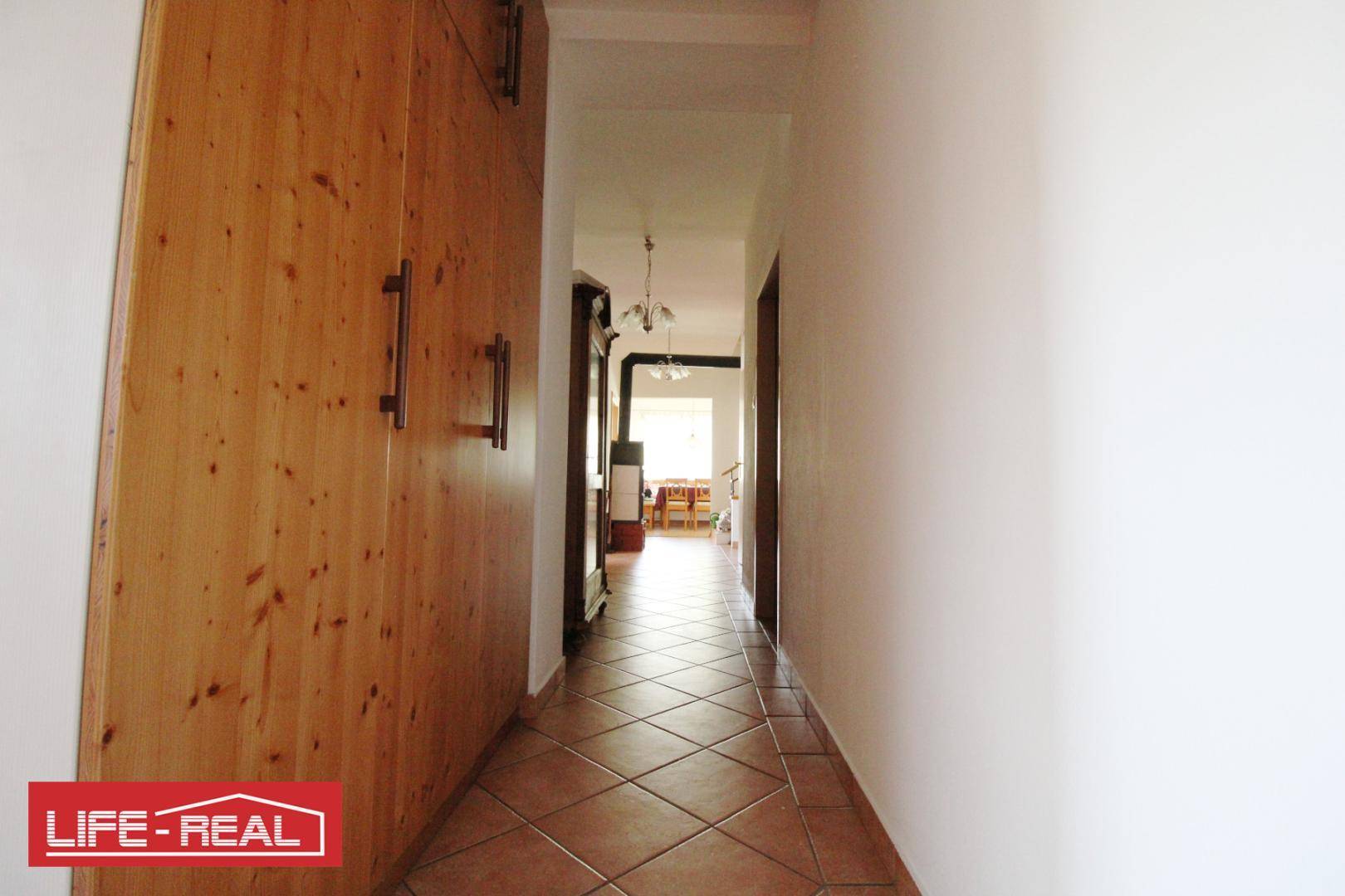 Langer Flur mit Holzschrank, Fliesenboden und Blick in einen weiteren Raum.