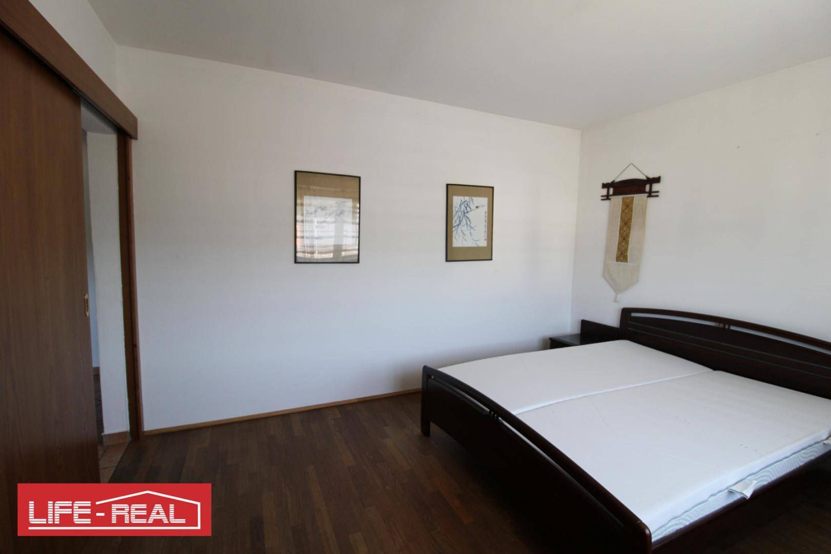 Schlafzimmer mit Holzboden, Doppelbett und Schiebetür.