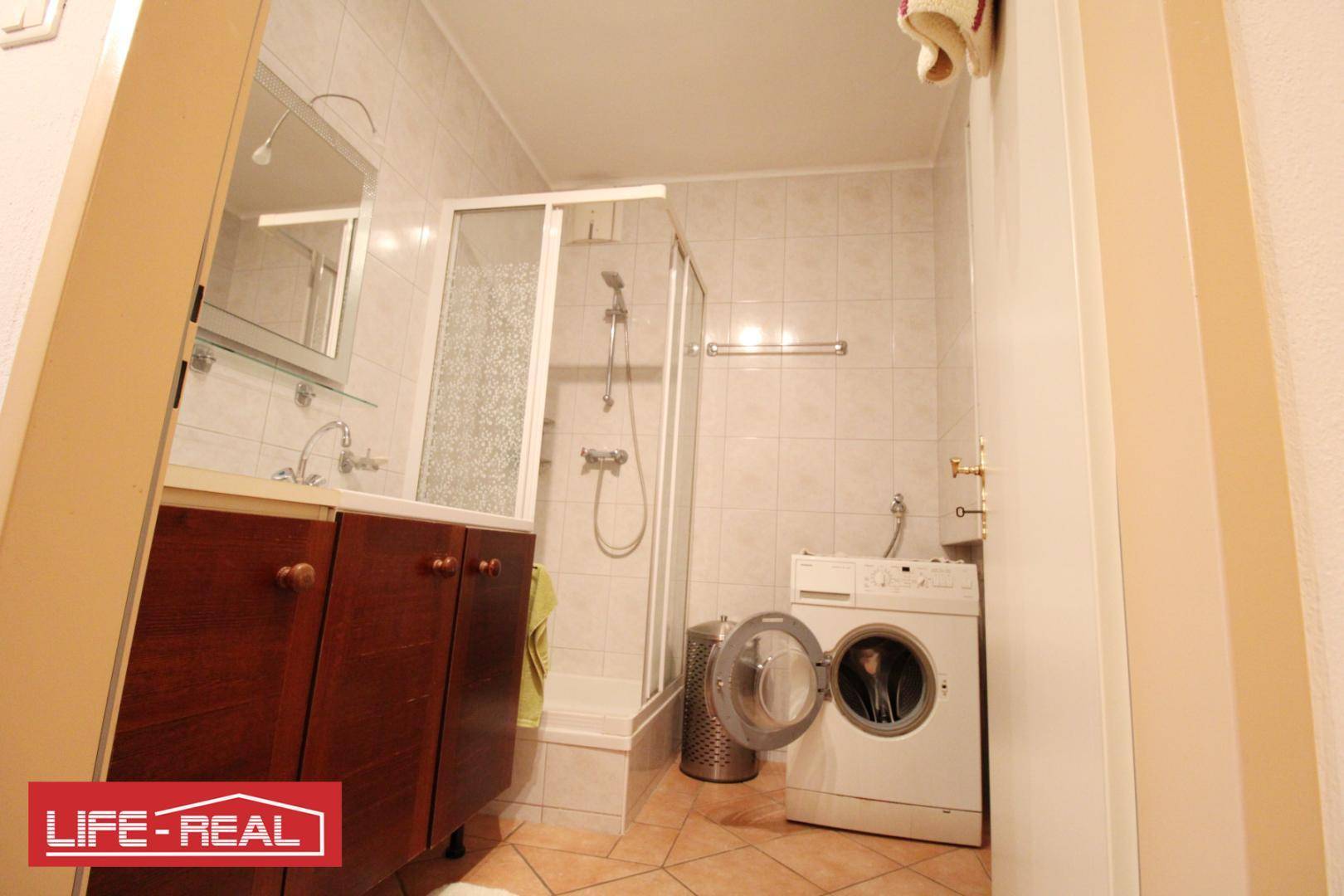 Kleines Badezimmer mit Dusche, Waschmaschine und Waschbecken.