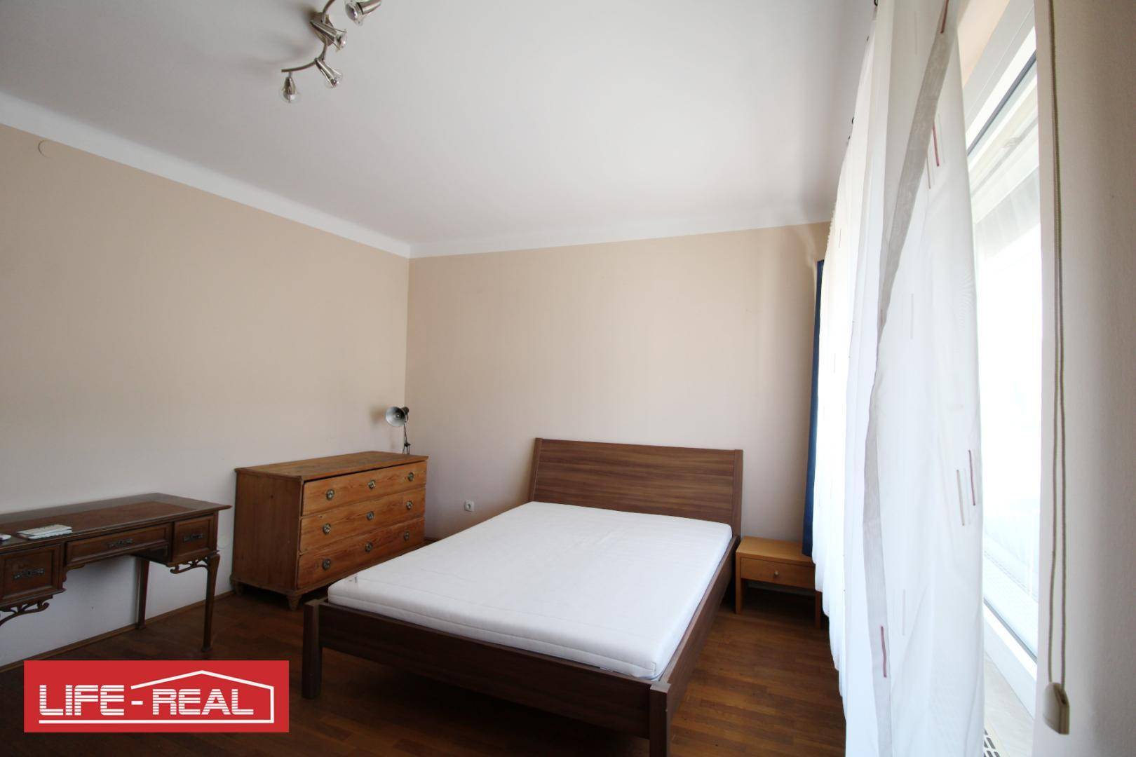 Helles Schlafzimmer mit Holzboden, Holzmöbeln und großem Fenster.