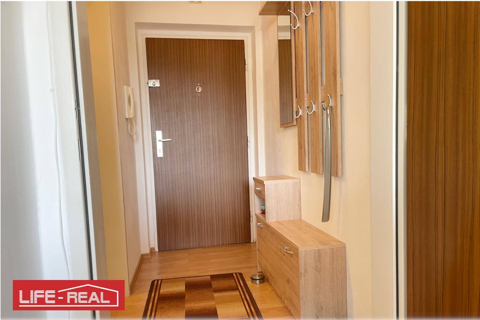 Heller Eingangsbereich mit Holztür, Garderobe und praktischen Schuhschränken.