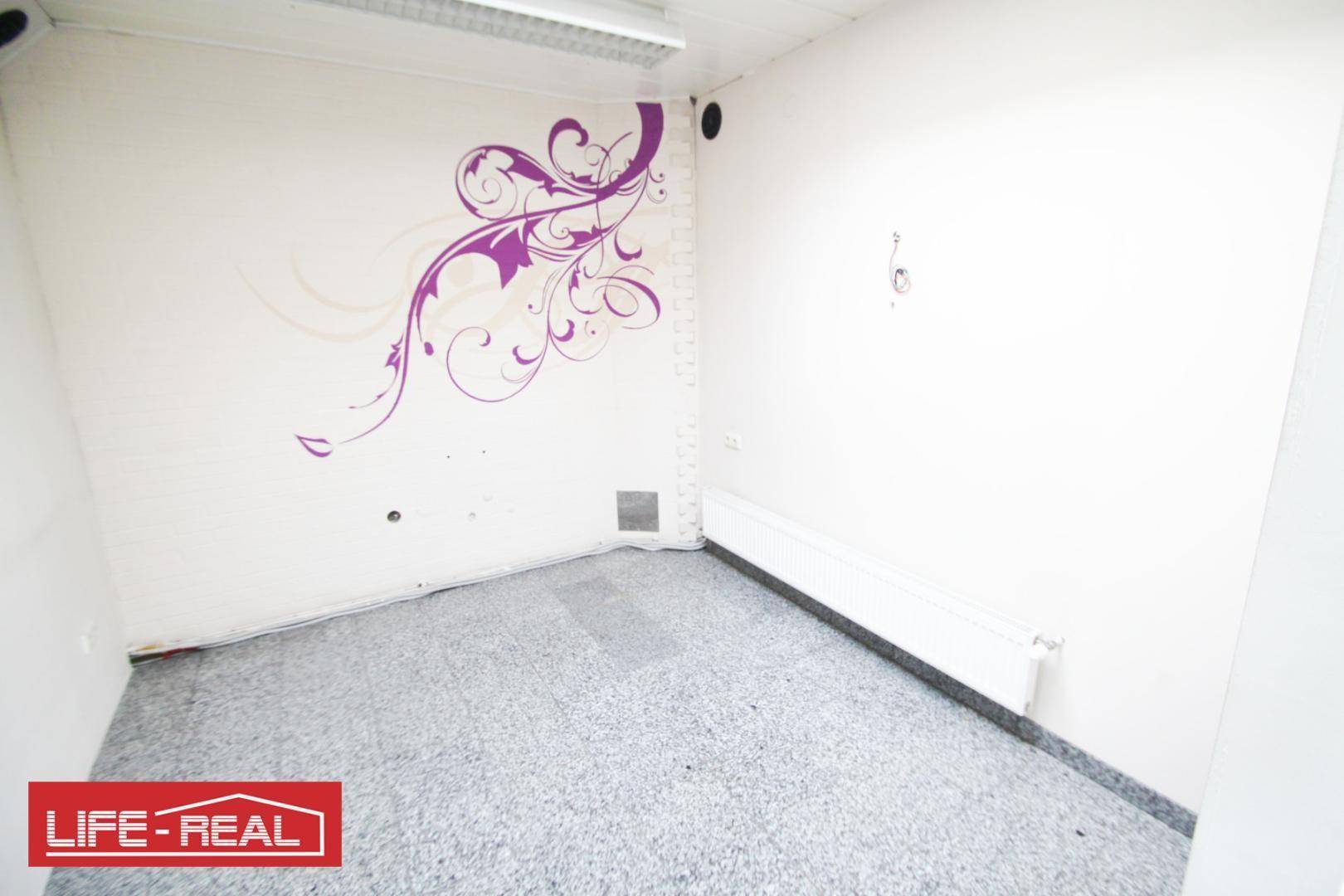 Kleinerer Büroraum mit Teppichboden, Heizkörper und lila Wanddekoration, ideal für Einzelbüro.