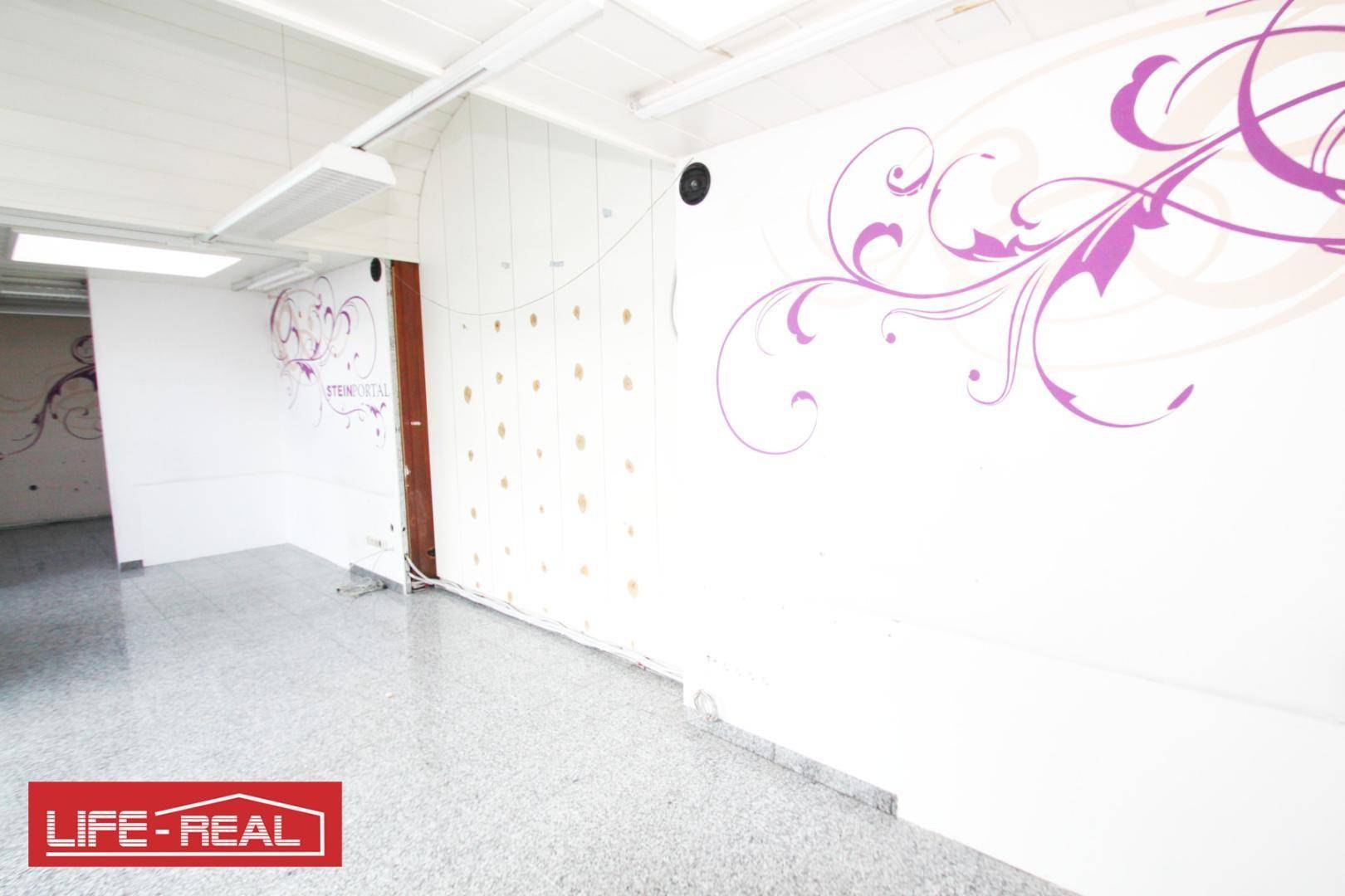 Heller Geschäftsraum mit weißer Wand, lila Wanddekoration und grauem Fliesenboden, bereit zur Nutzung.