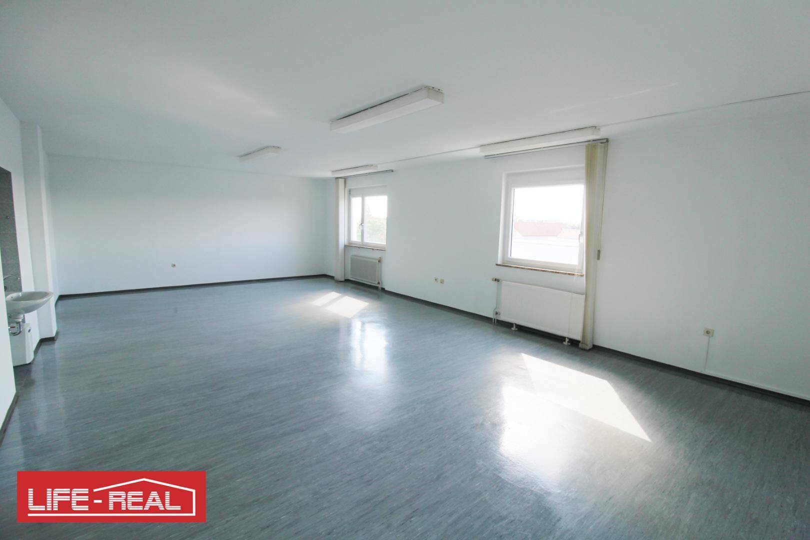 Großer, heller Büroraum mit zwei Fenstern, Heizkörpern und viel Tageslicht, ideal für gewerbliche Nutzung.