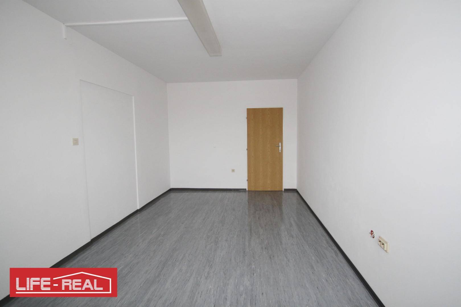 Schlichter, leerer Raum mit weiß gestrichenen Wänden und einer Holztür, vielseitig nutzbar.