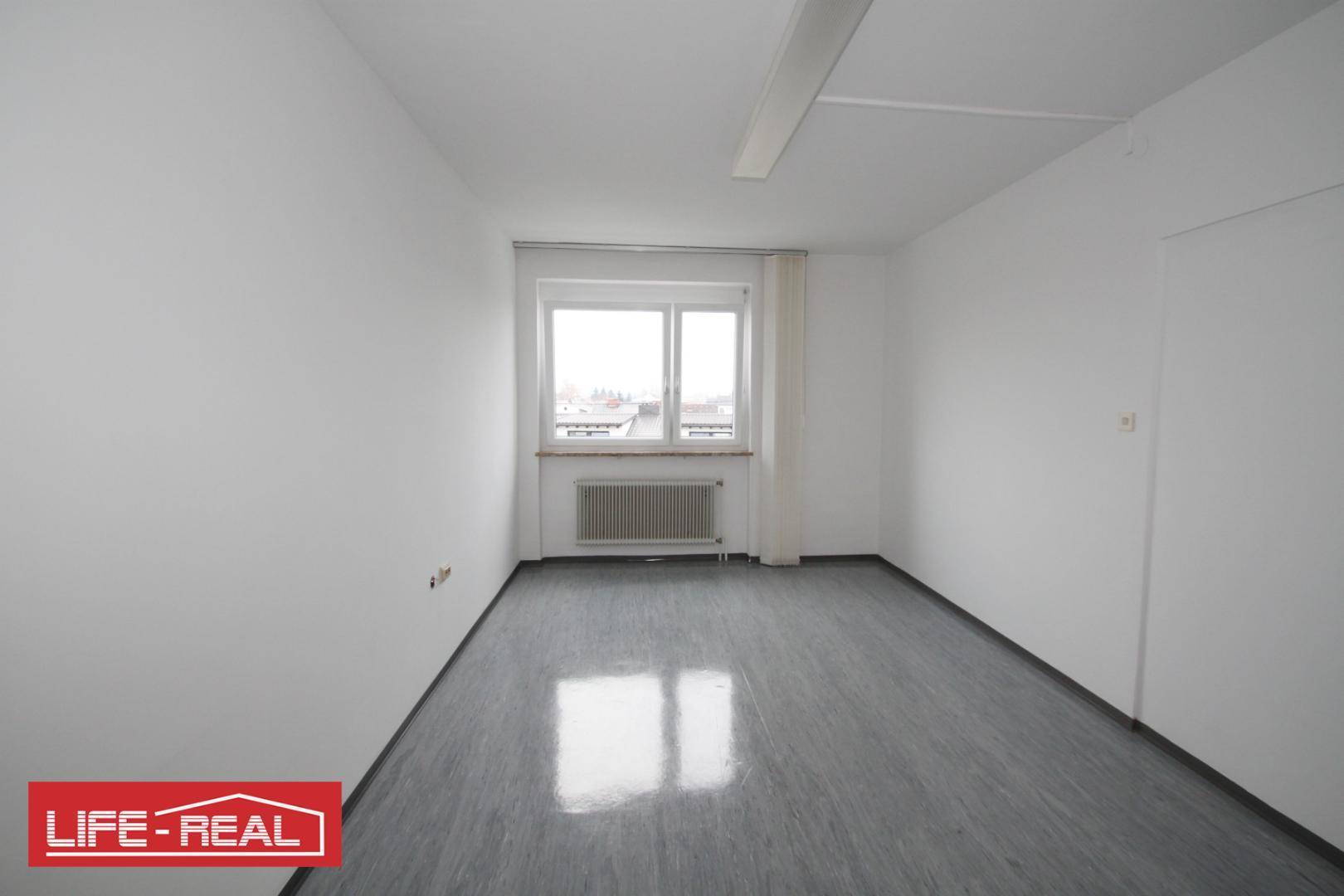 Kleinerer, heller Raum mit einem großen Fenster und Heizkörper, ideal als Einzelbüro oder Lager.