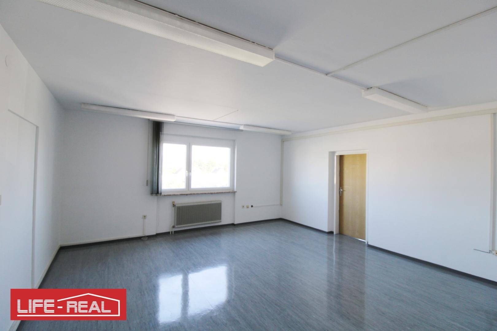Heller, leerer Raum mit glänzendem Boden, einem Fenster, Heizkörper und einer hellen Holztür.