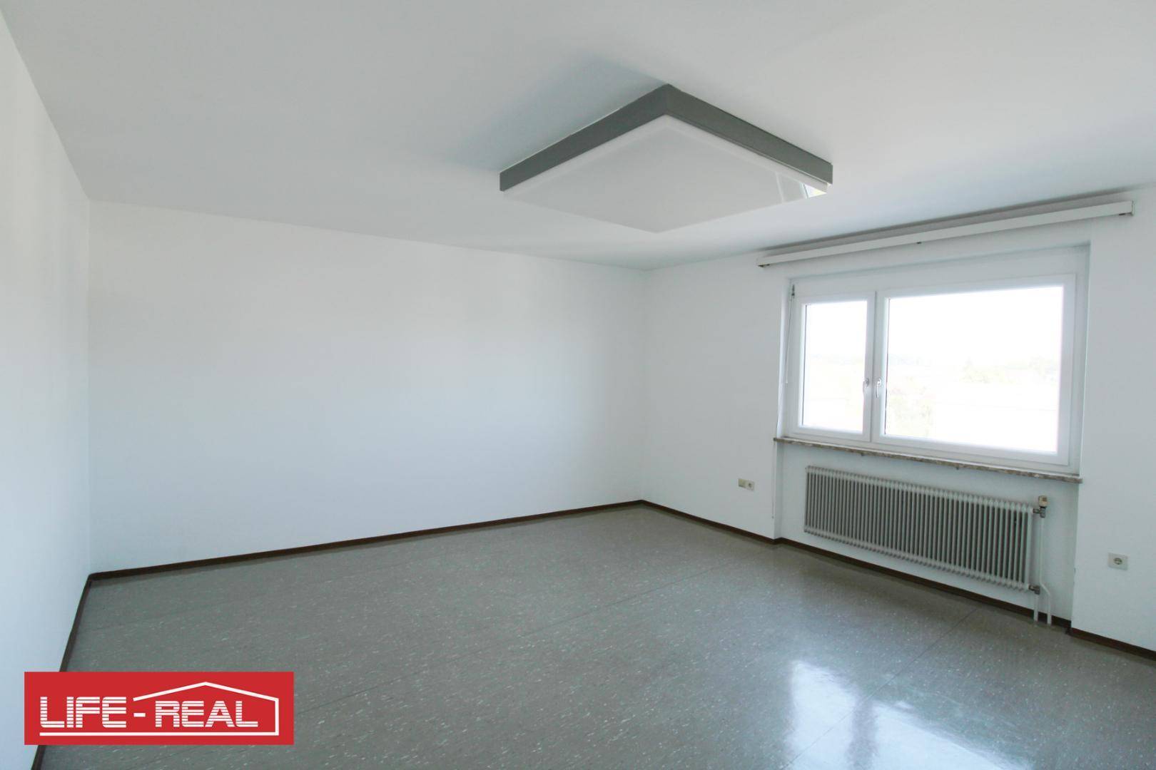 Leerer Raum mit weiß gestrichenen Wänden, einem Fenster und einem modernen Deckenlicht.