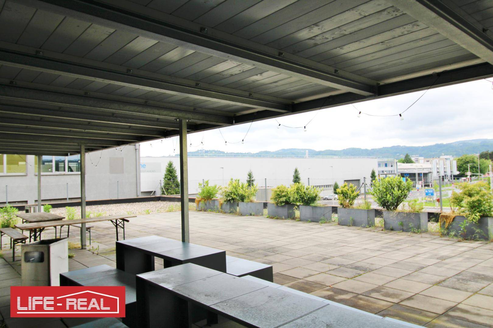 Überdachte Terrasse mit Blick auf die Umgebung, ausgestattet mit Sitzbänken und Pflanzen, ideal für entspannte Pausen.
